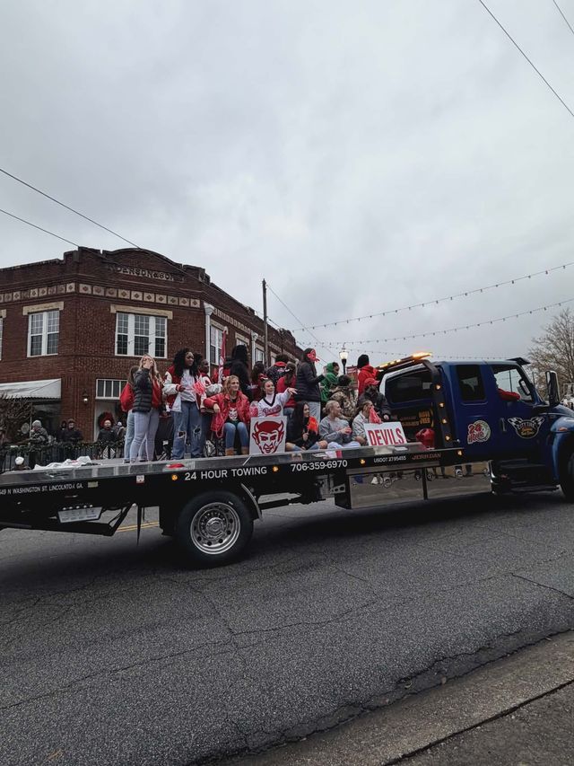 People on a flatbed truck float in a parade, brick buildings in background, overcast day.