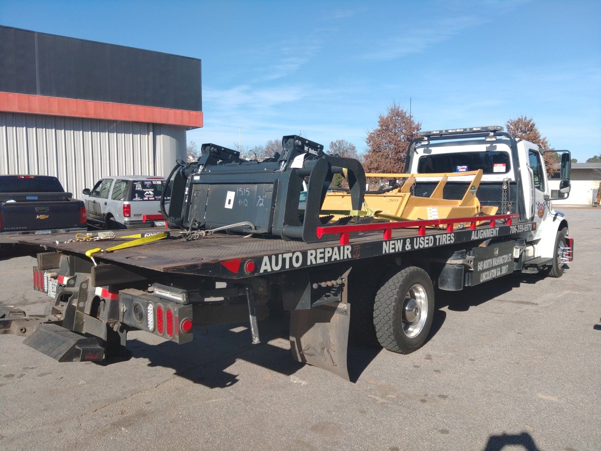 Tow truck with auto repair signage carrying equipment on a sunny day.