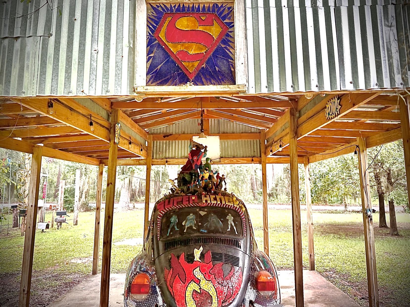 A car with a superman logo on the front is under a wooden structure.