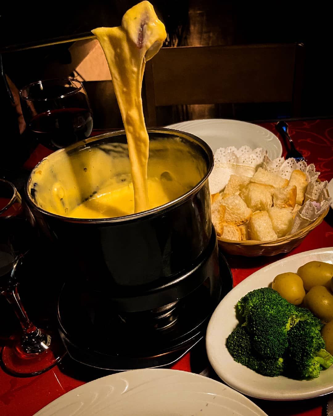 Uma pessoa está mergulhando um pedaço de queijo em uma panela de fondue Gramado Serra Gaúcha