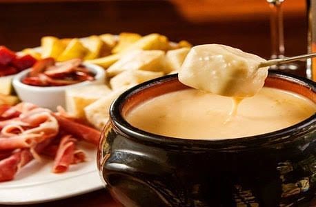 Uma pessoa está mergulhando um pedaço de queijo em uma tigela de fondue Gramado Serra Gaúcha