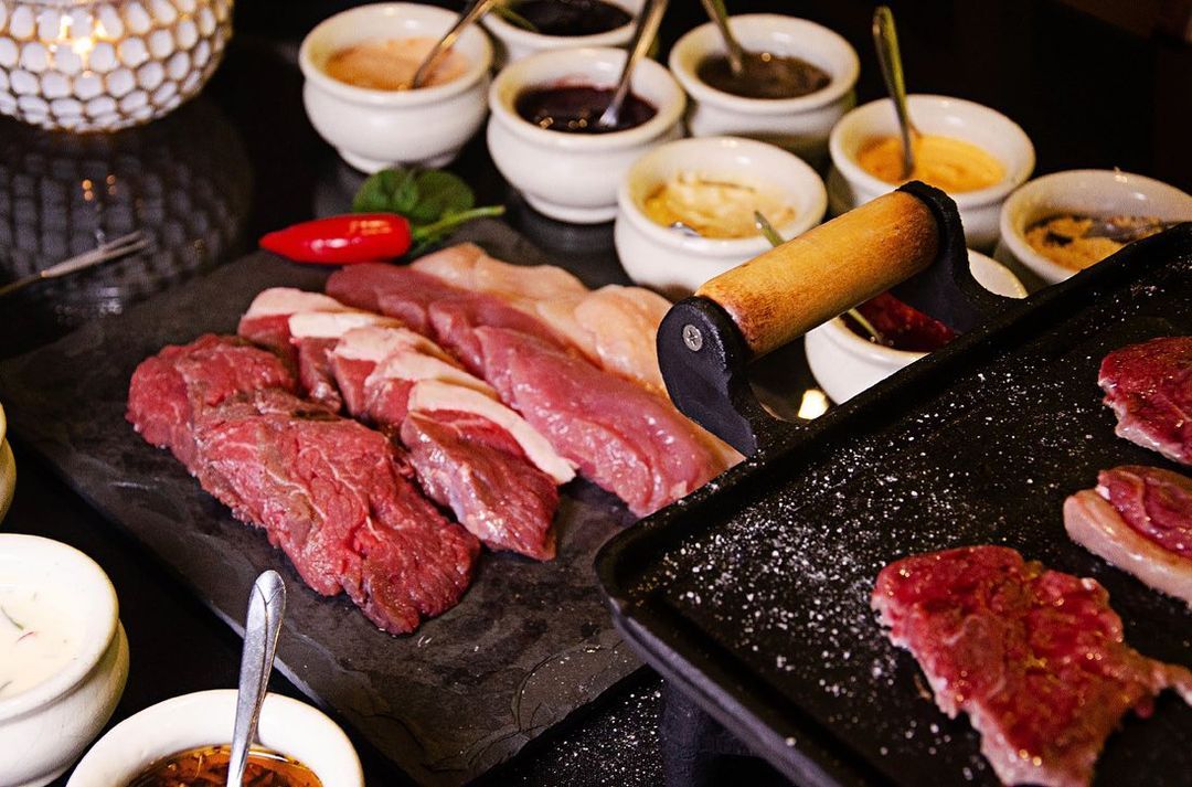 Uma mesa coberta com uma variedade de carnes e molhos fondue Gramado Serra Gaúcha