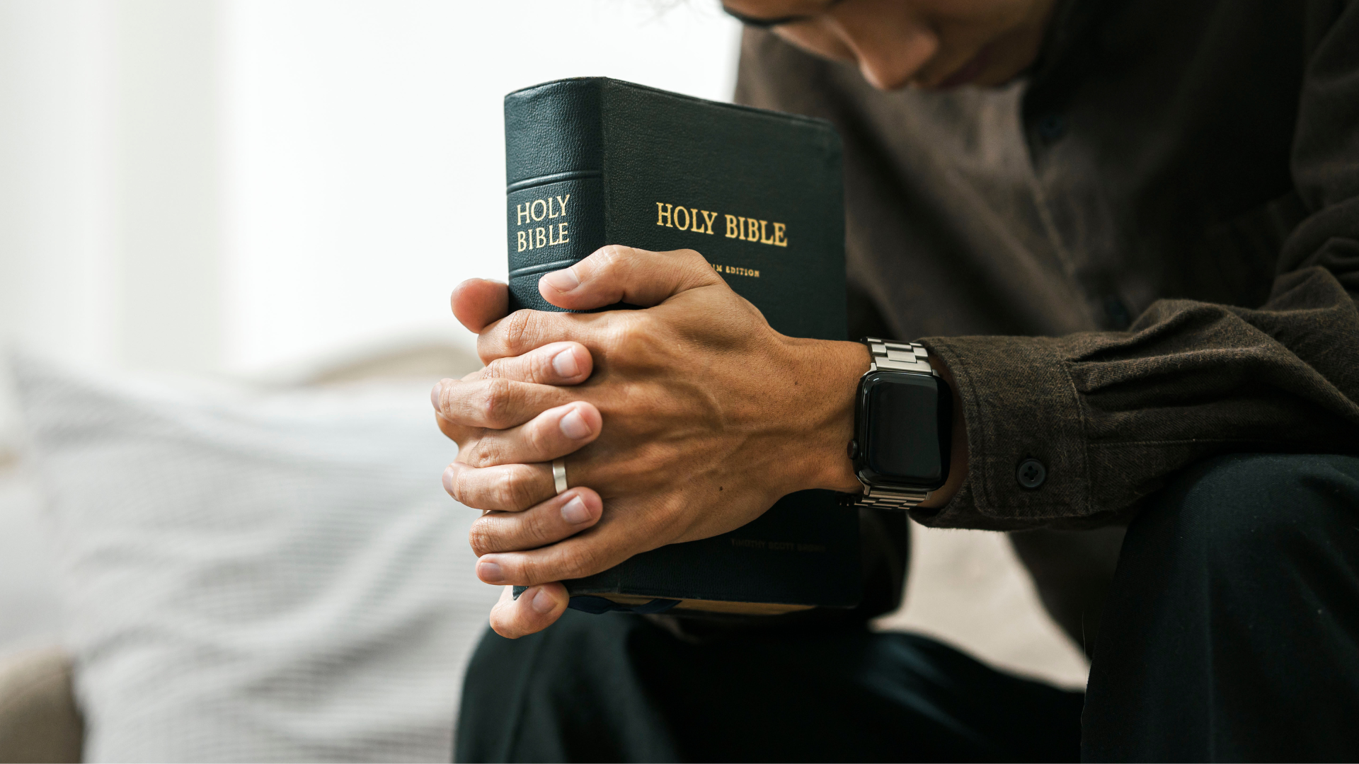 Person holding a Bible, head bowed in prayer, hands clasped.