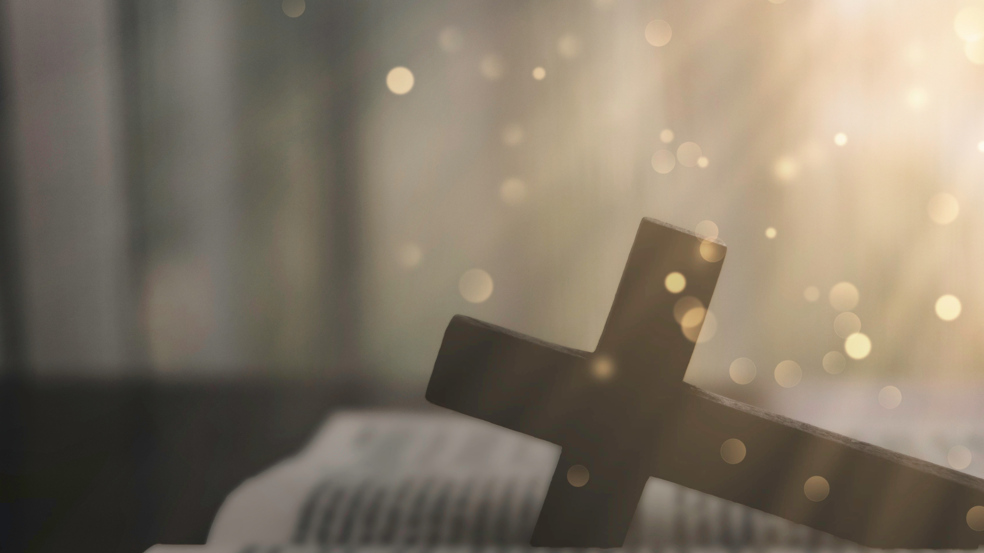 Wooden cross on an open book, with soft light and bokeh in the background.