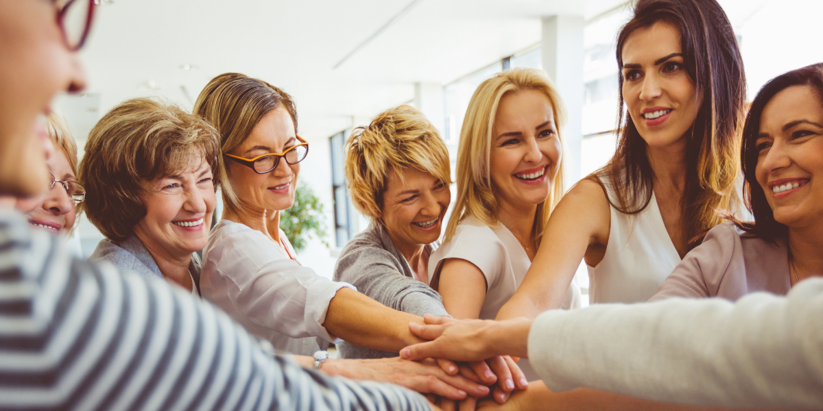 Group of women with hands stacked together, smiling.