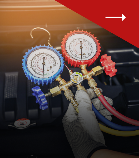 A gloved hand holds an automotive AC manifold gauge set with red, blue, and yellow hoses over a car engine.