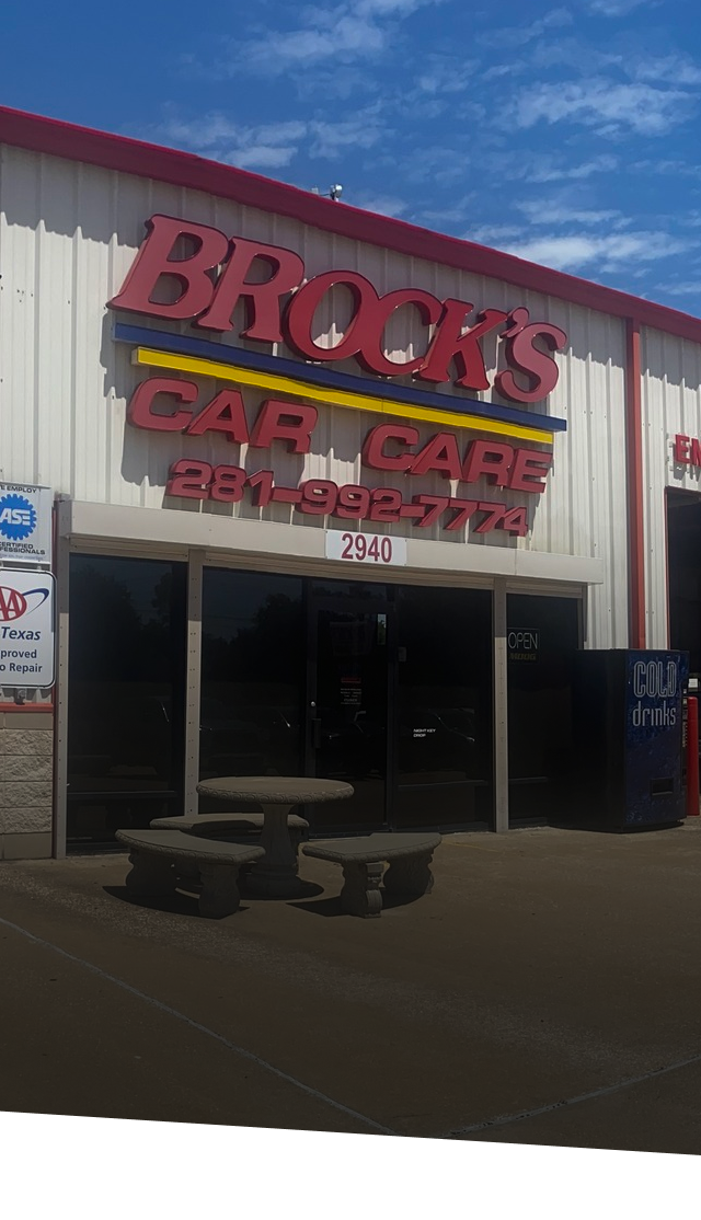 The storefront of Brock's Car Care, with red and blue lettering, a concrete table set, and a blue vending machine.