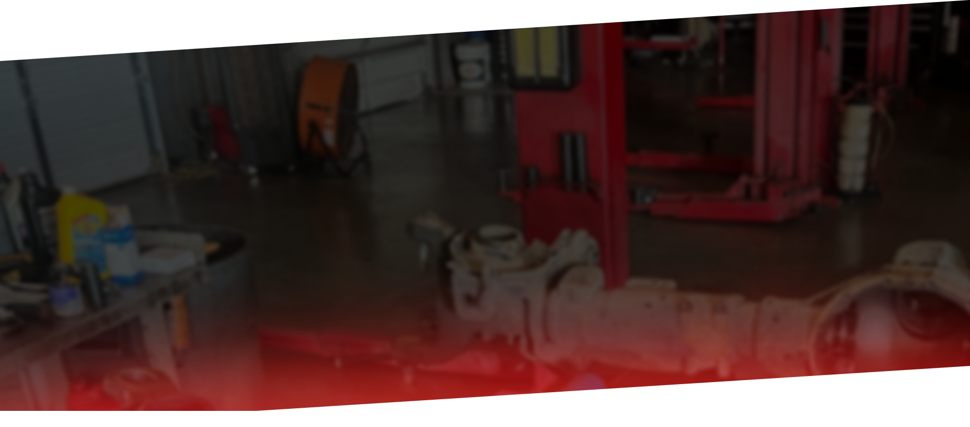 A view of a messy automotive repair shop with a large car axle assembly resting on the concrete floor.