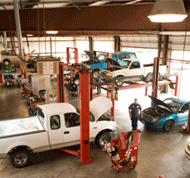A mechanic works inside an auto repair shop with multiple vehicles on lifts.