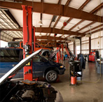 An interior view of an auto repair shop with multiple vehicles, red car lifts, and equipment on a concrete floor.