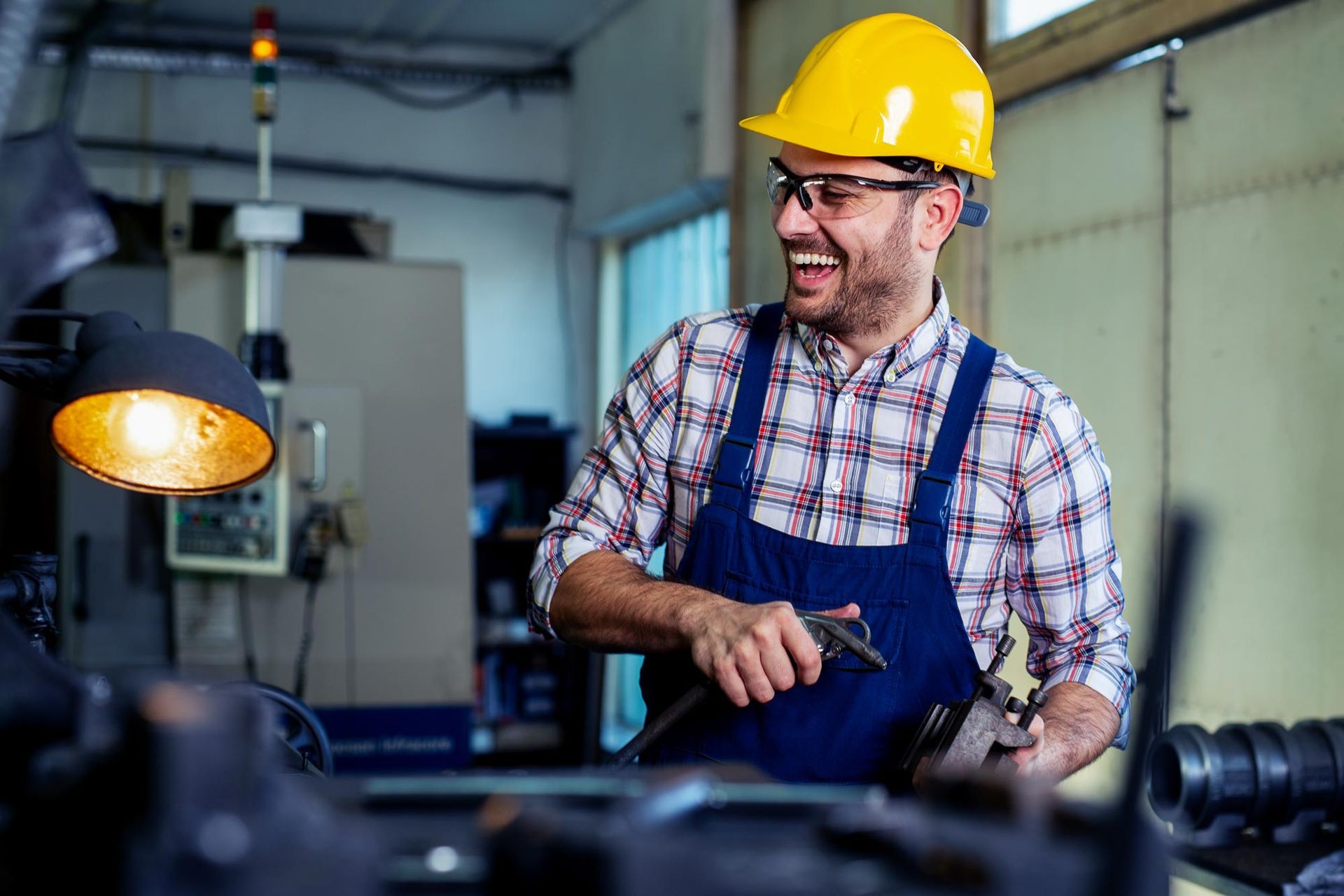 A man wearing a hard hat and safety glasses is working in a factory.