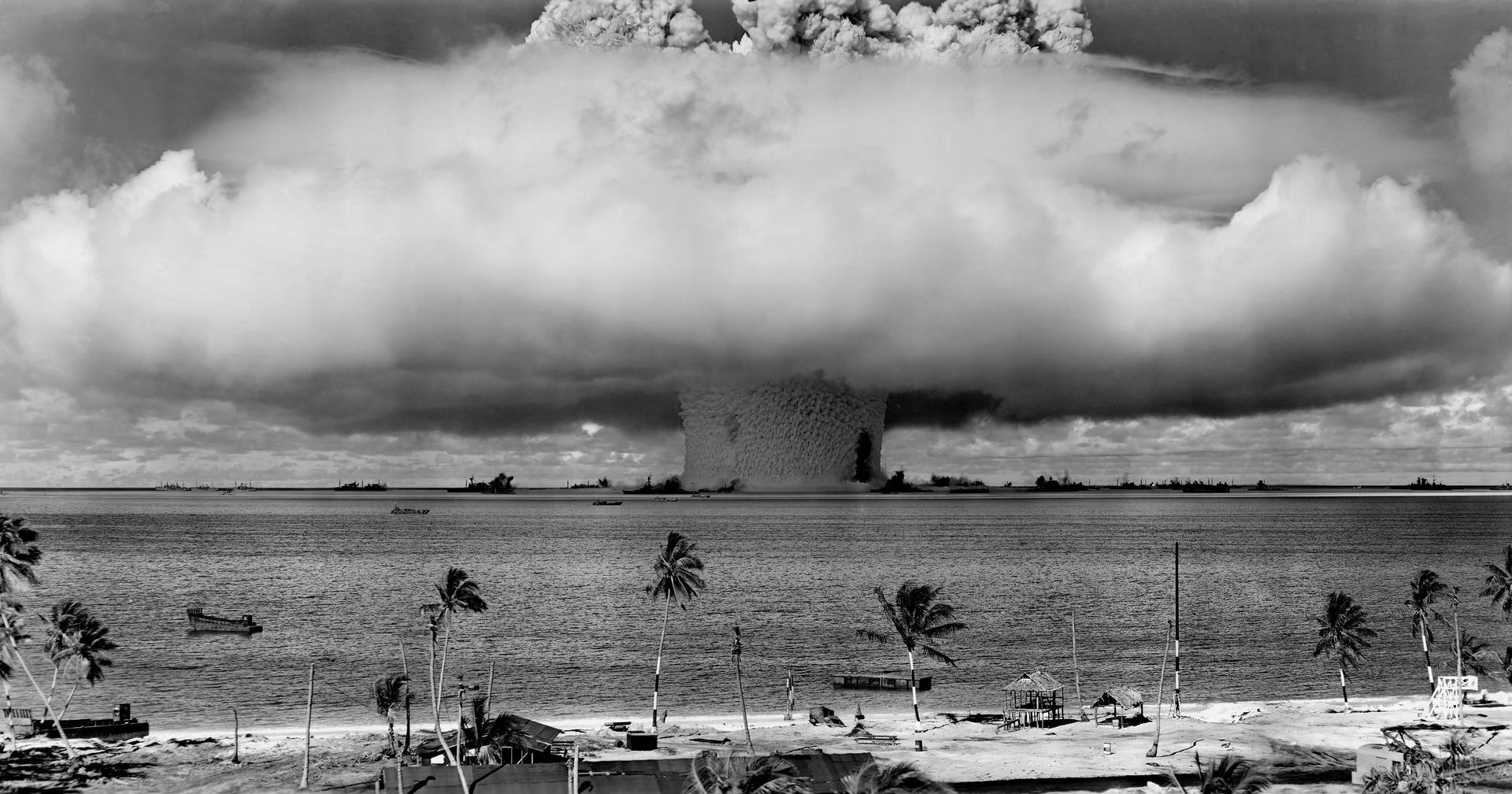 Black-and-white nuclear explosion mushroom cloud rising over a flat landscape with smoke and debris