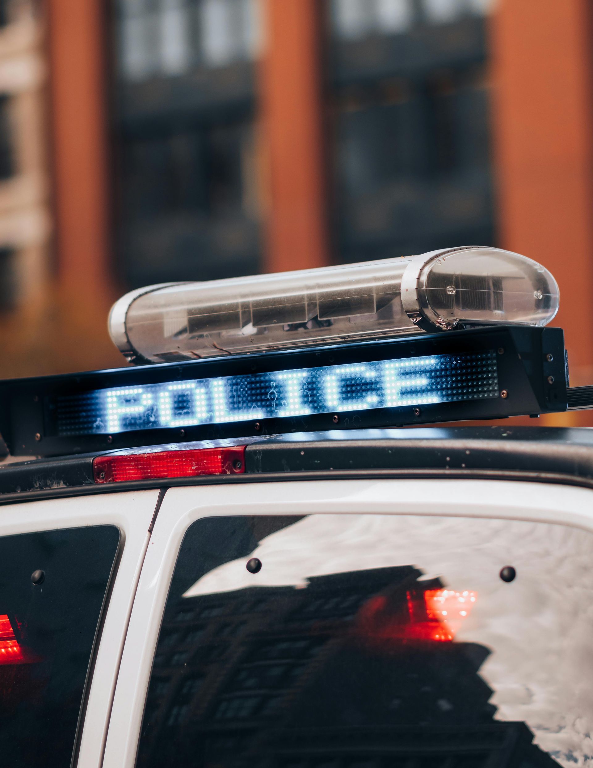 Police car with flashing blue lights and rooftop light bar, parked in an urban street.