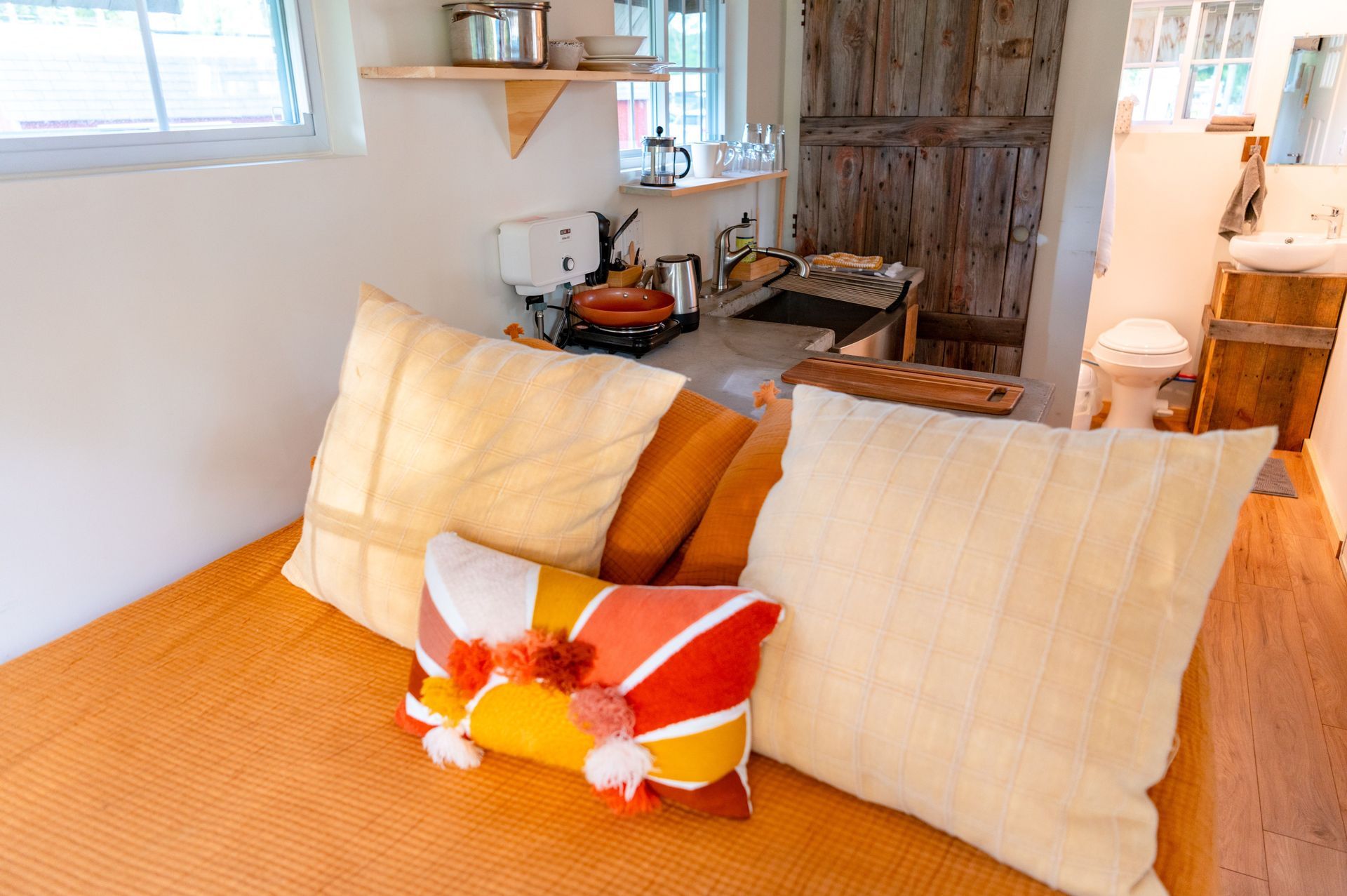 Interior of a tiny home in Texas with a built-in daybed, cushions, and a compact kitchen along the back wall