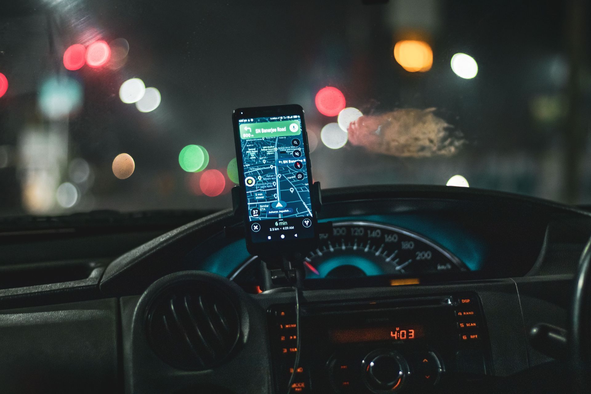 Smartphone mounted on a car dashboard running a driving app at night, illustrating usage-based insurance tracking