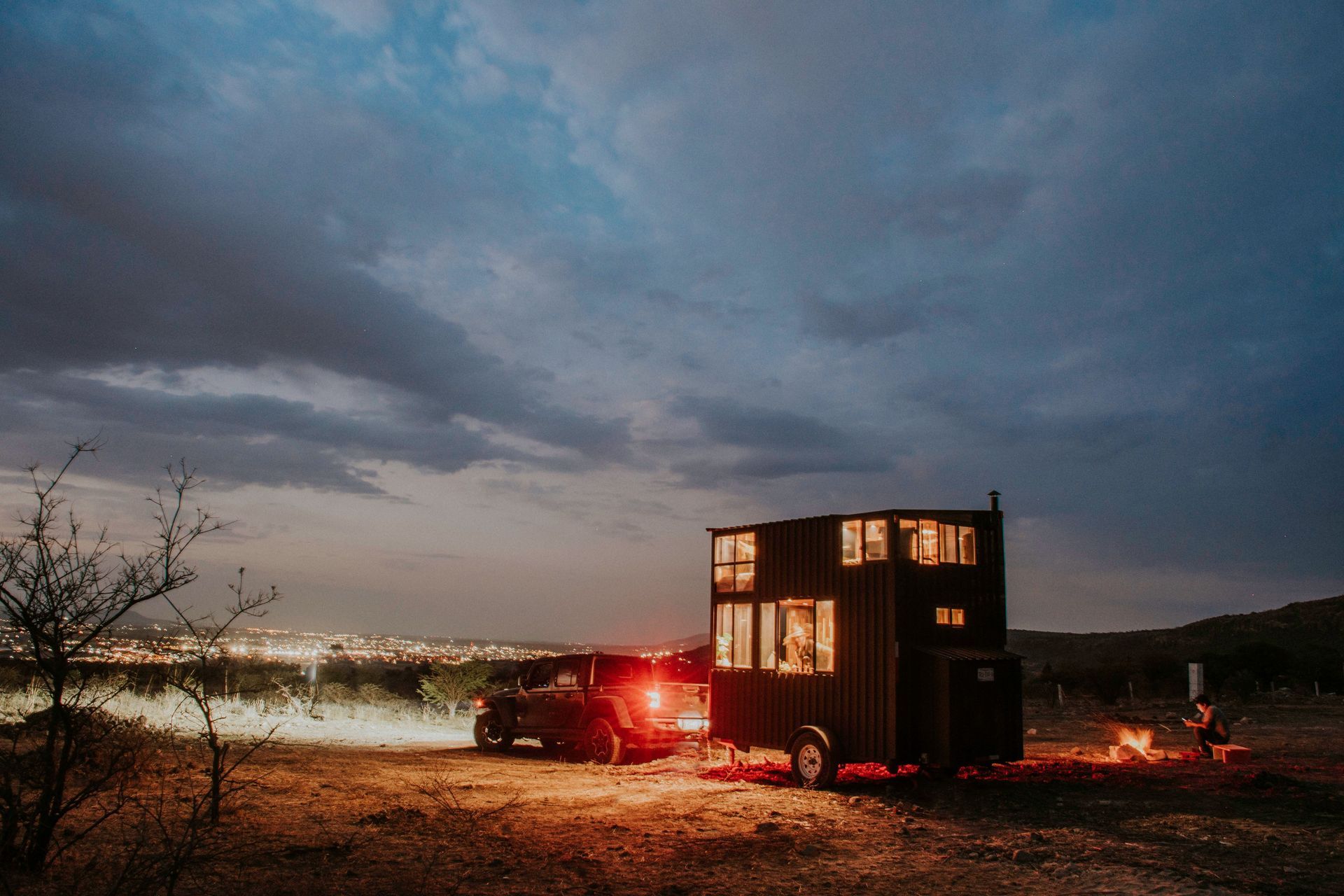 Tiny home on a trailer parked on open North Texas land at dusk with a pickup truck and storm clouds