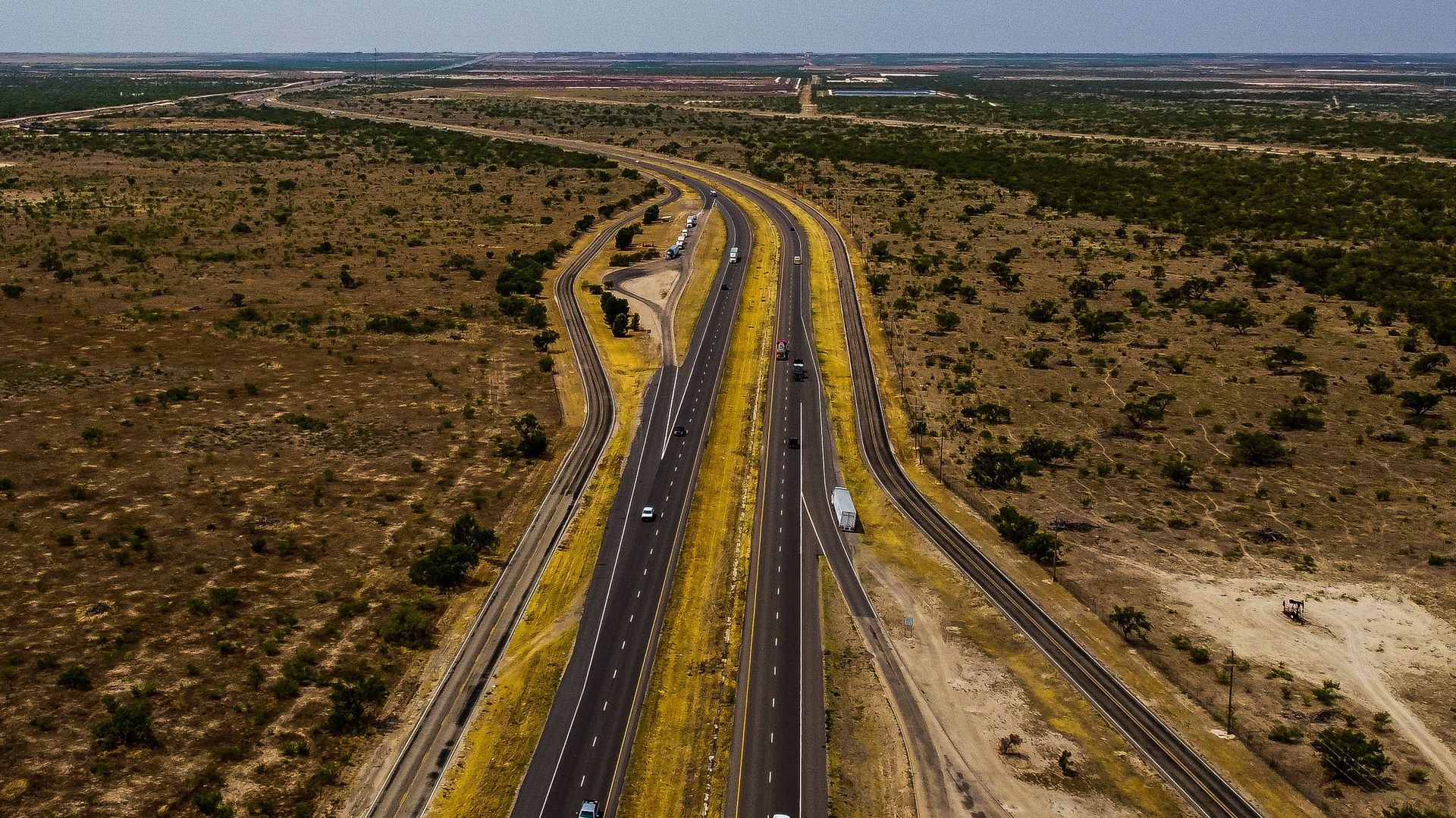 Aerial view of a divided North Texas highway cutting through flat mesquite scrubland under a wide cl
