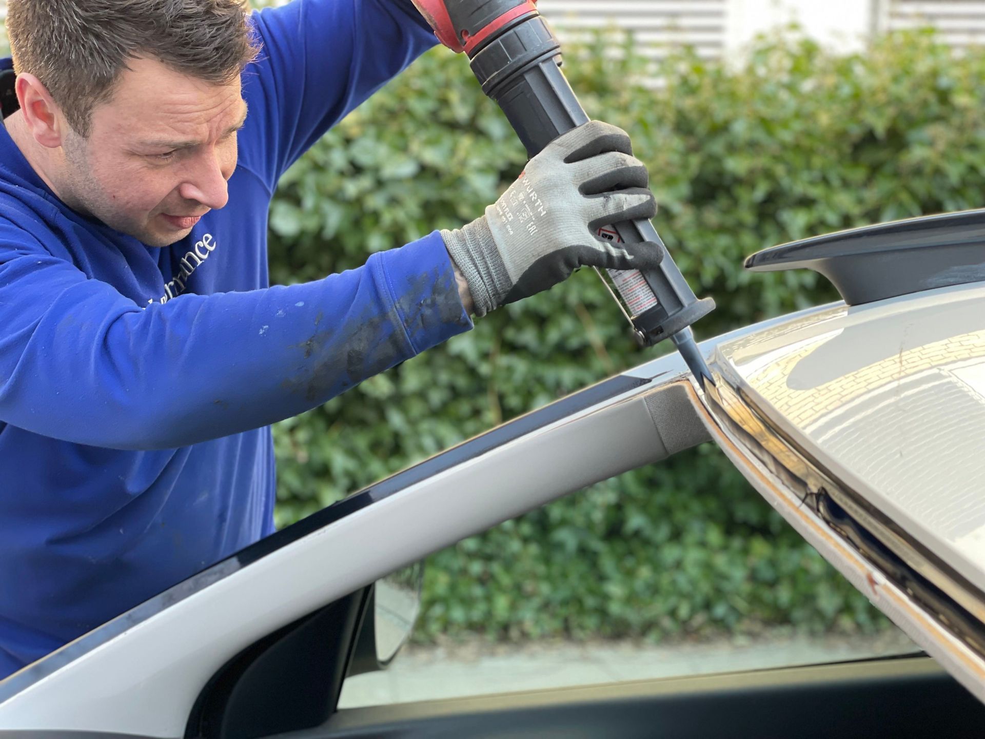 An auto glass technician running a bead of urethane adhesive along a car's windshield frame before setting the new glass