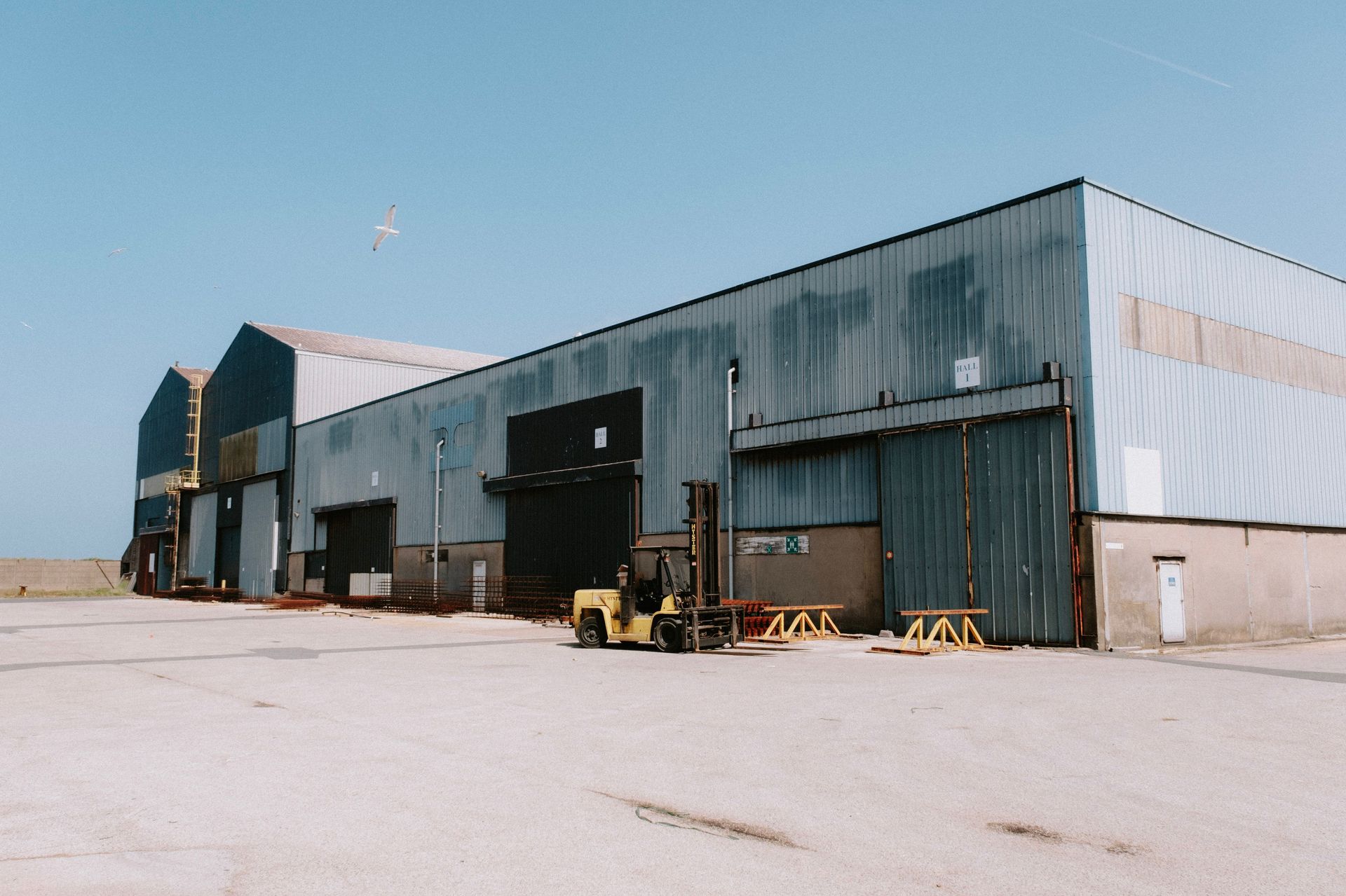 A tractor-trailer backed up to a metal warehouse on a flat sunny lot, a typical two-truck yard