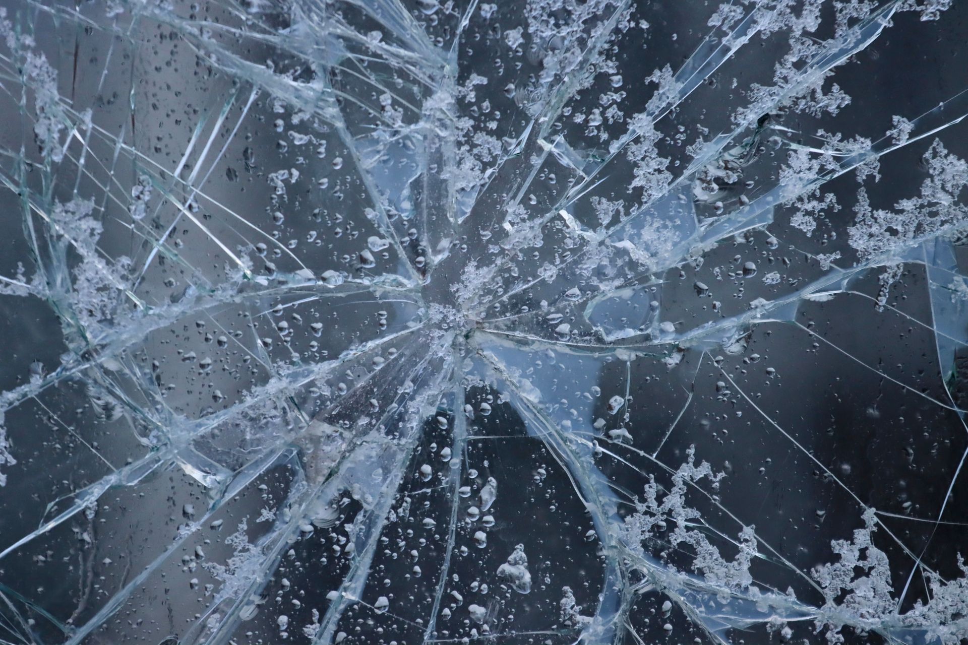 Close-up of cracks spreading out from a rock impact point across a dark car windshield in Texas