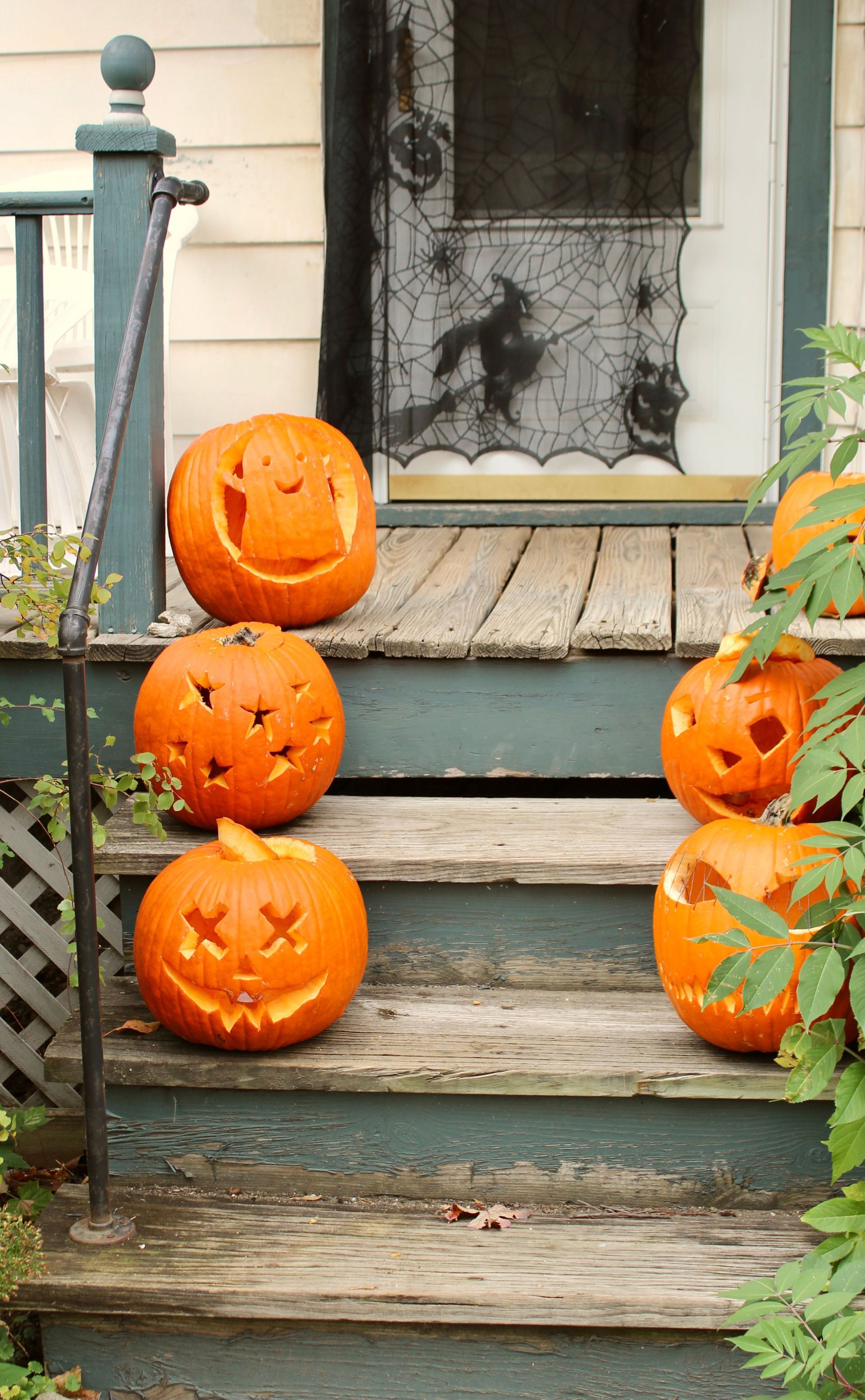 Carved jack-o-lanterns lined up on worn wooden porch steps beside a handrail, right where a trick-or-treater could trip