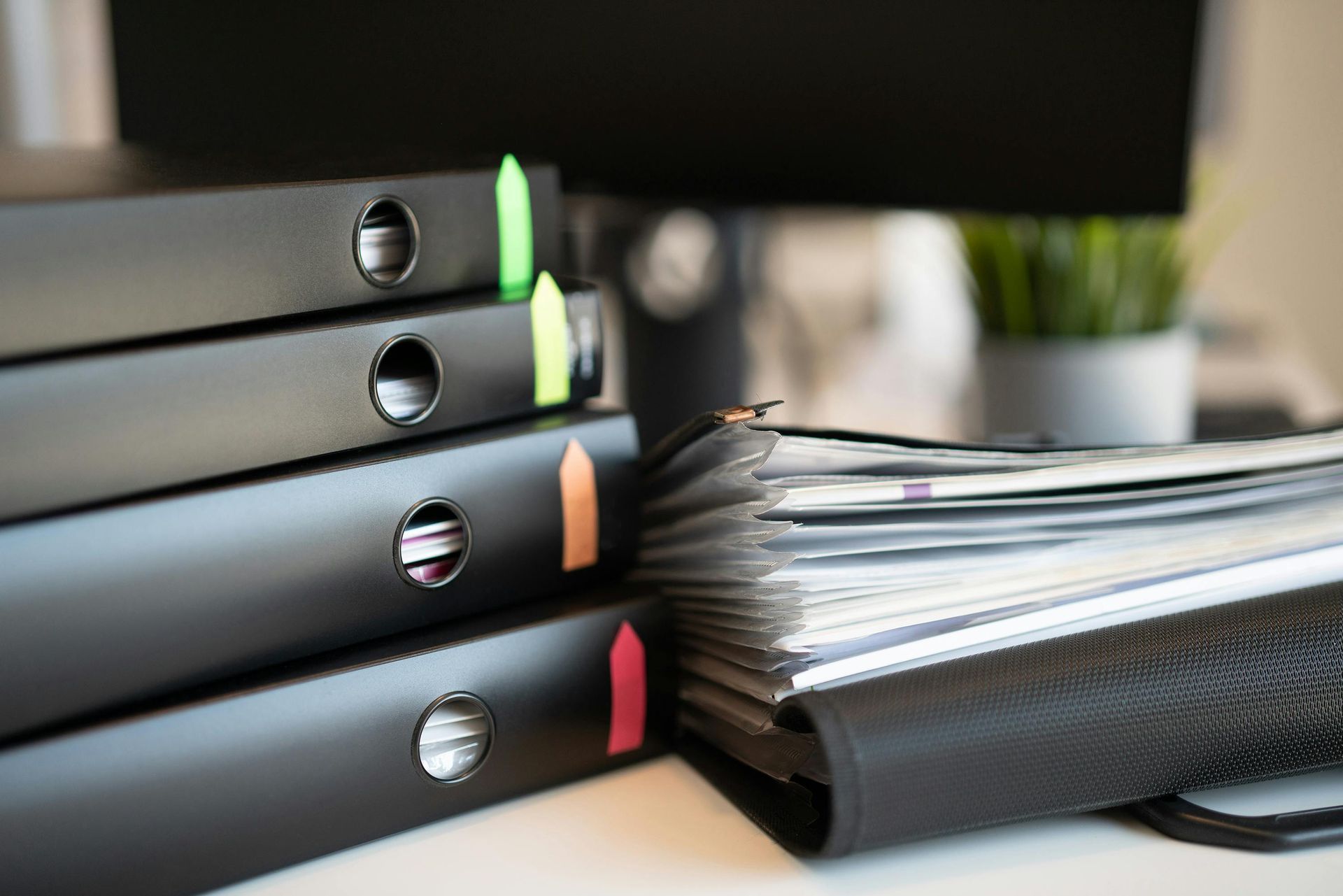 Stacked binders and a thick notebook on a desk, with colorful tabs and pages fanned open
