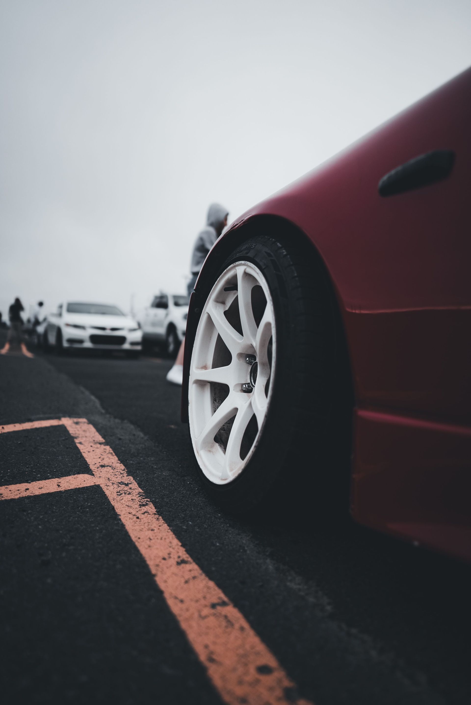 Close-up of a parked dark red car's front wheel and fender on an asphalt lot in Texas daylight