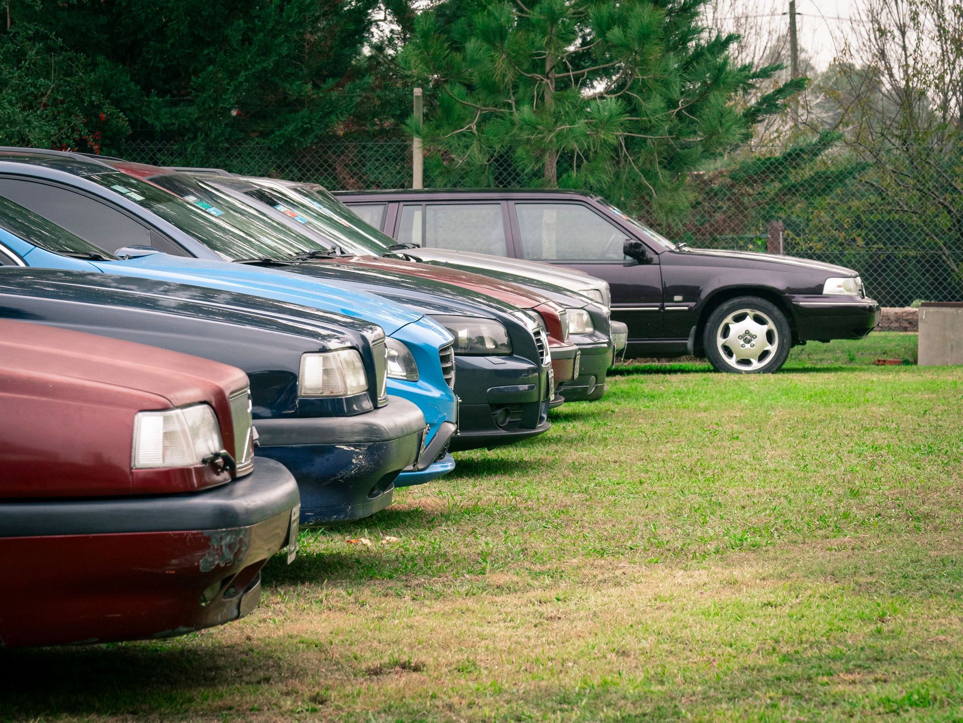 A row of customer vehicles parked along a fence line at a storage lot, the garagekeepers exposure back at the yard