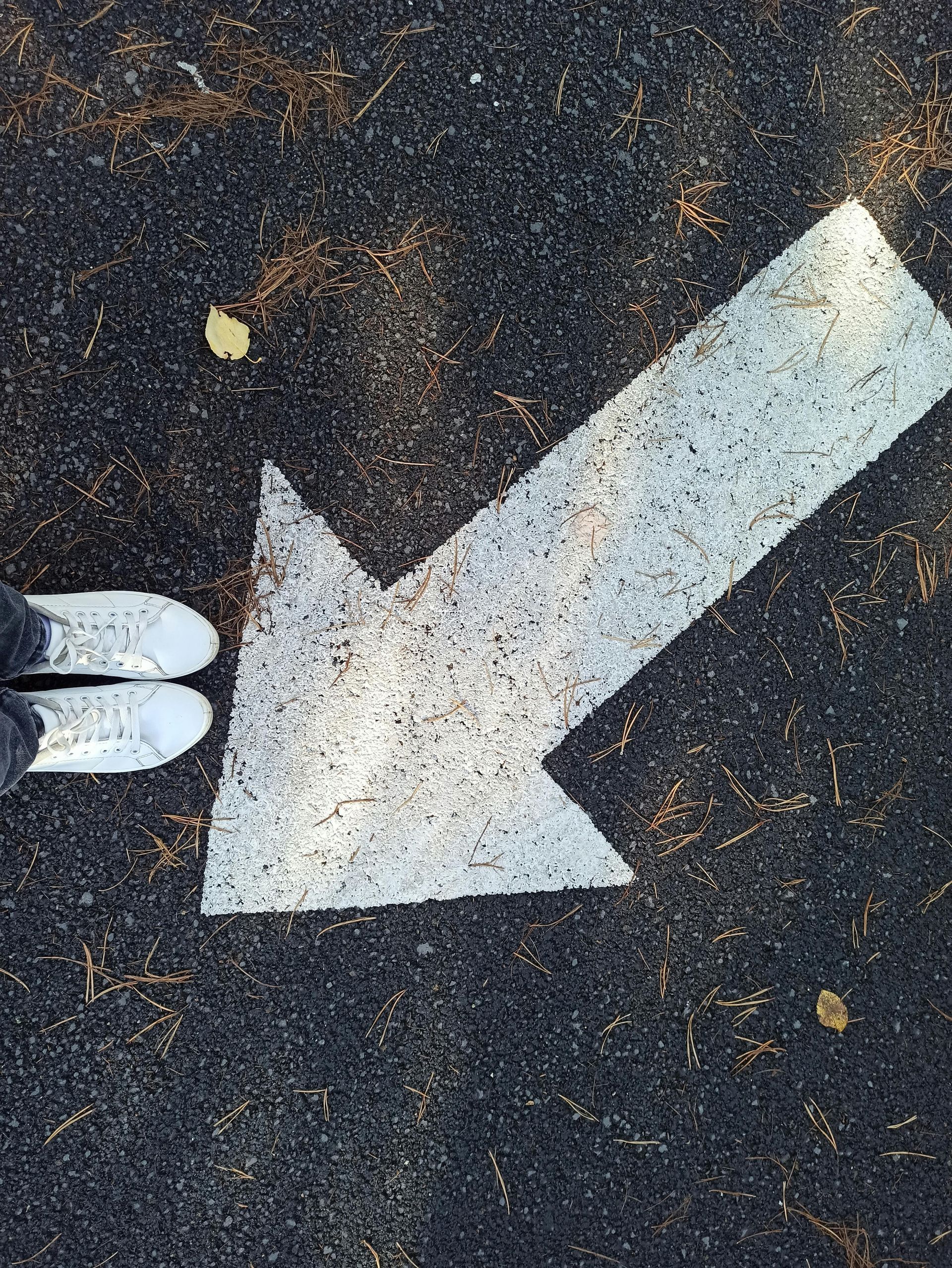 White arrow painted on dark pavement, pointing left, with white shoes at the edge.