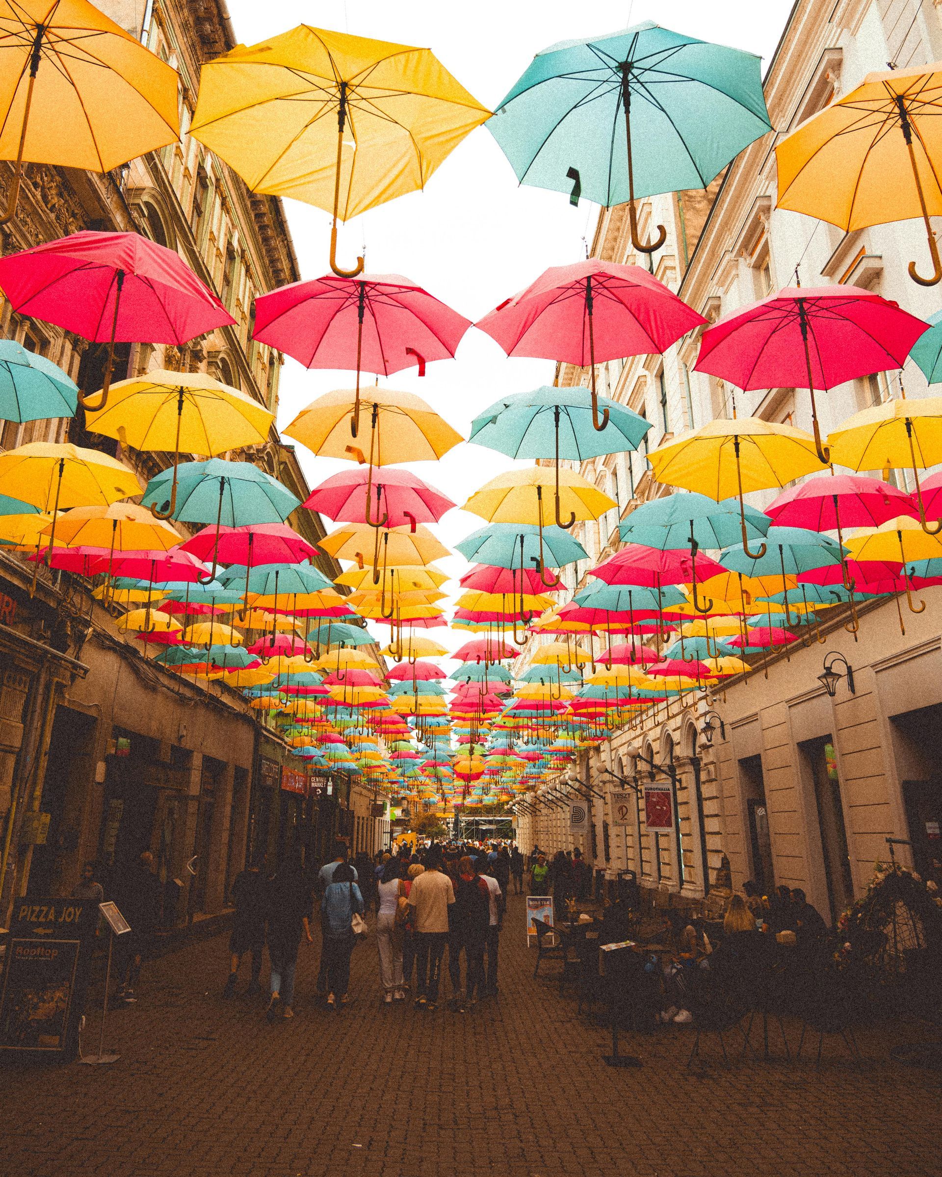 Colorful umbrellas hanging overhead above a narrow street with people walking below