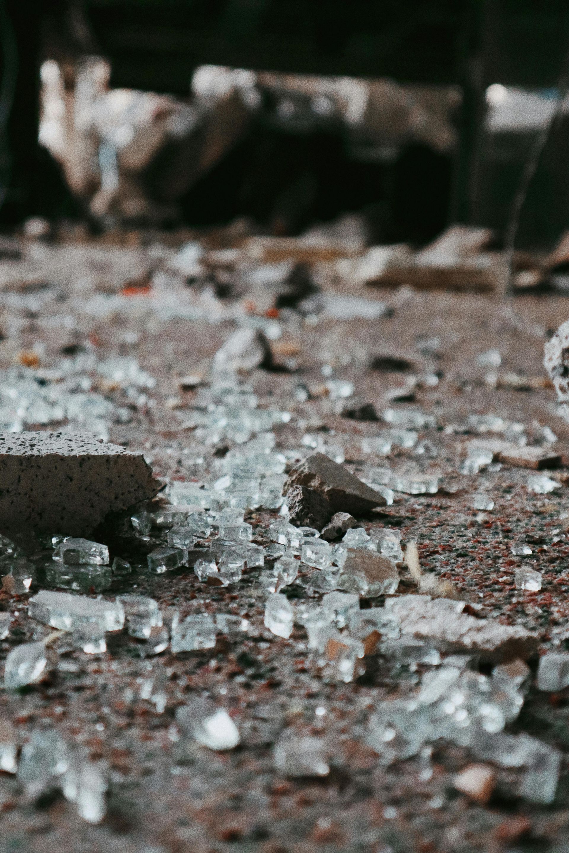 Broken glass scattered on a floor near a brick edge, with debris in the background