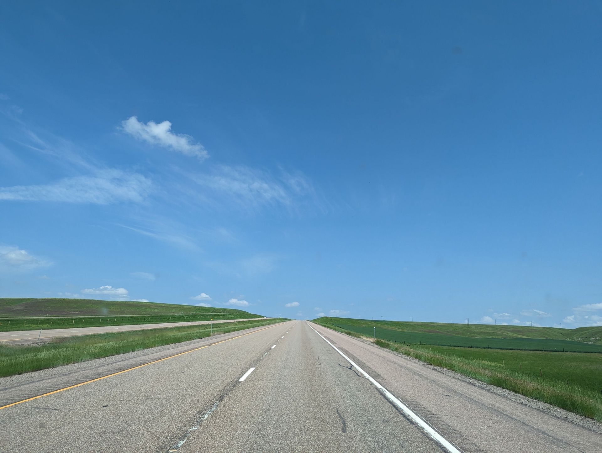 Empty two-lane highway running straight across flat open prairie under a blue sky, the road a hotshot rig takes into Oklahoma