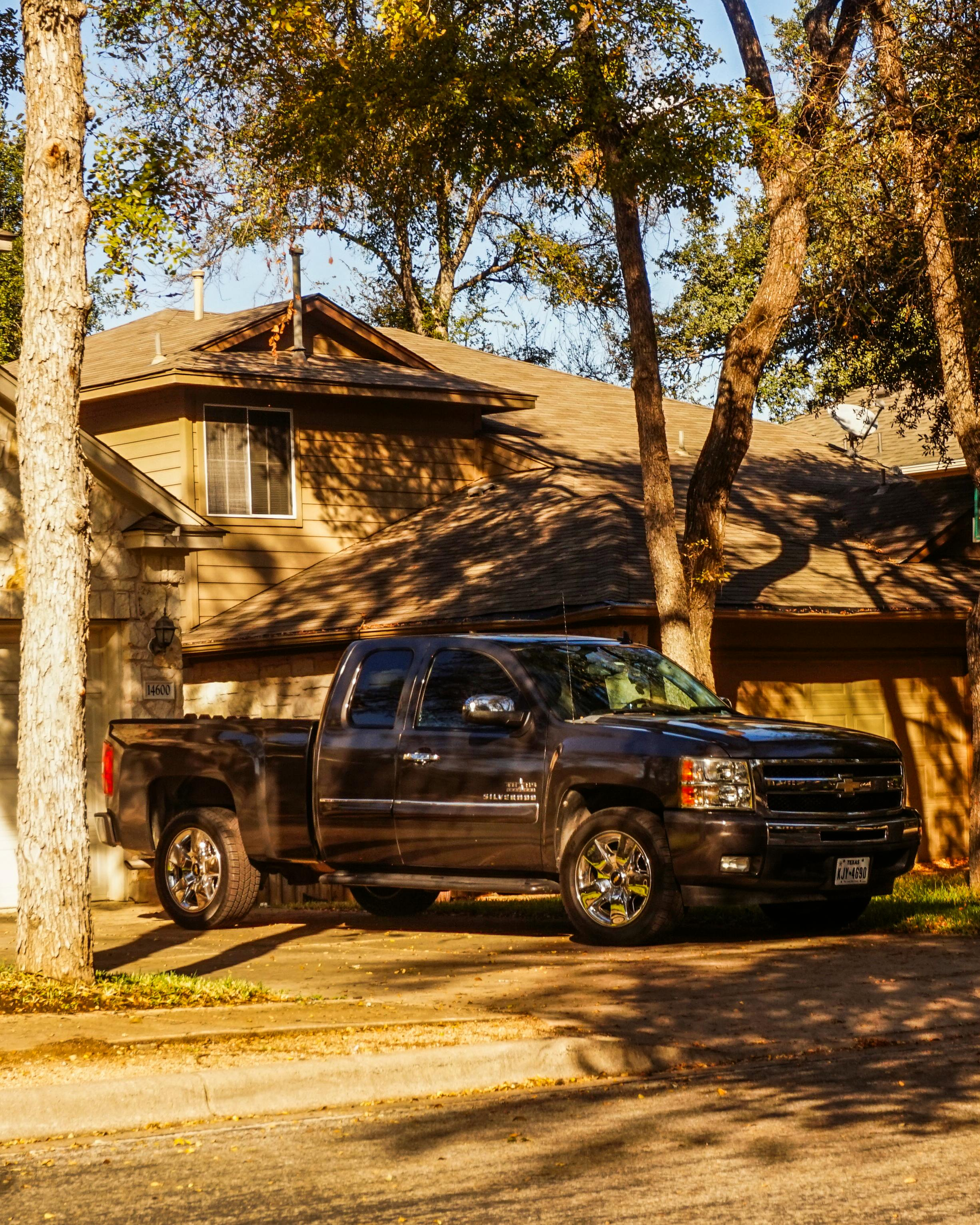 Dark pickup truck parked in front of a tan house with trees and autumn sunlight