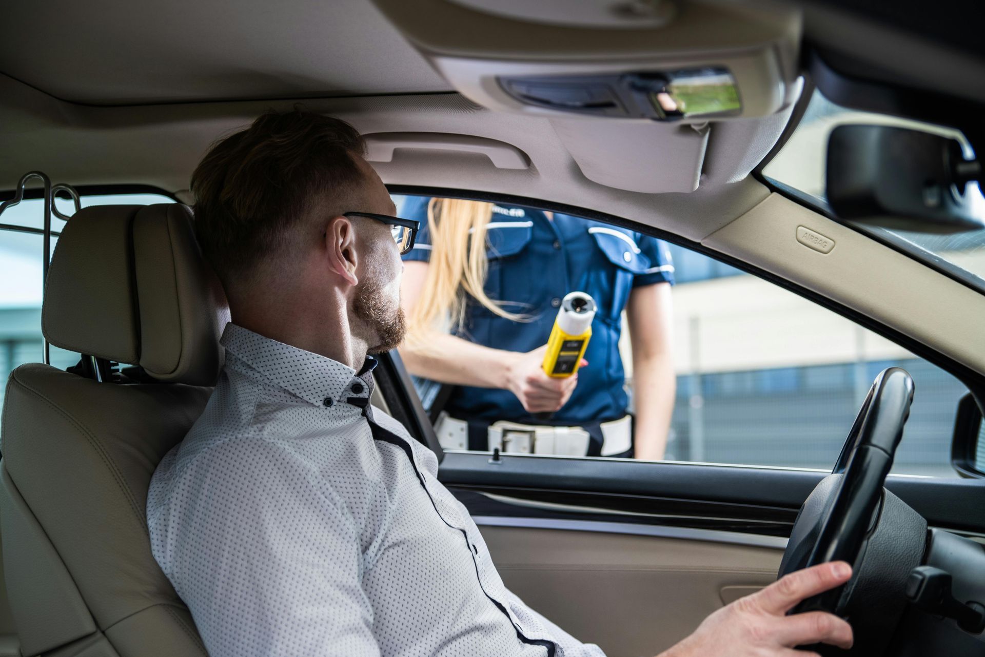 Driver blowing into breathalyzer at roadside stop with officer outside car window