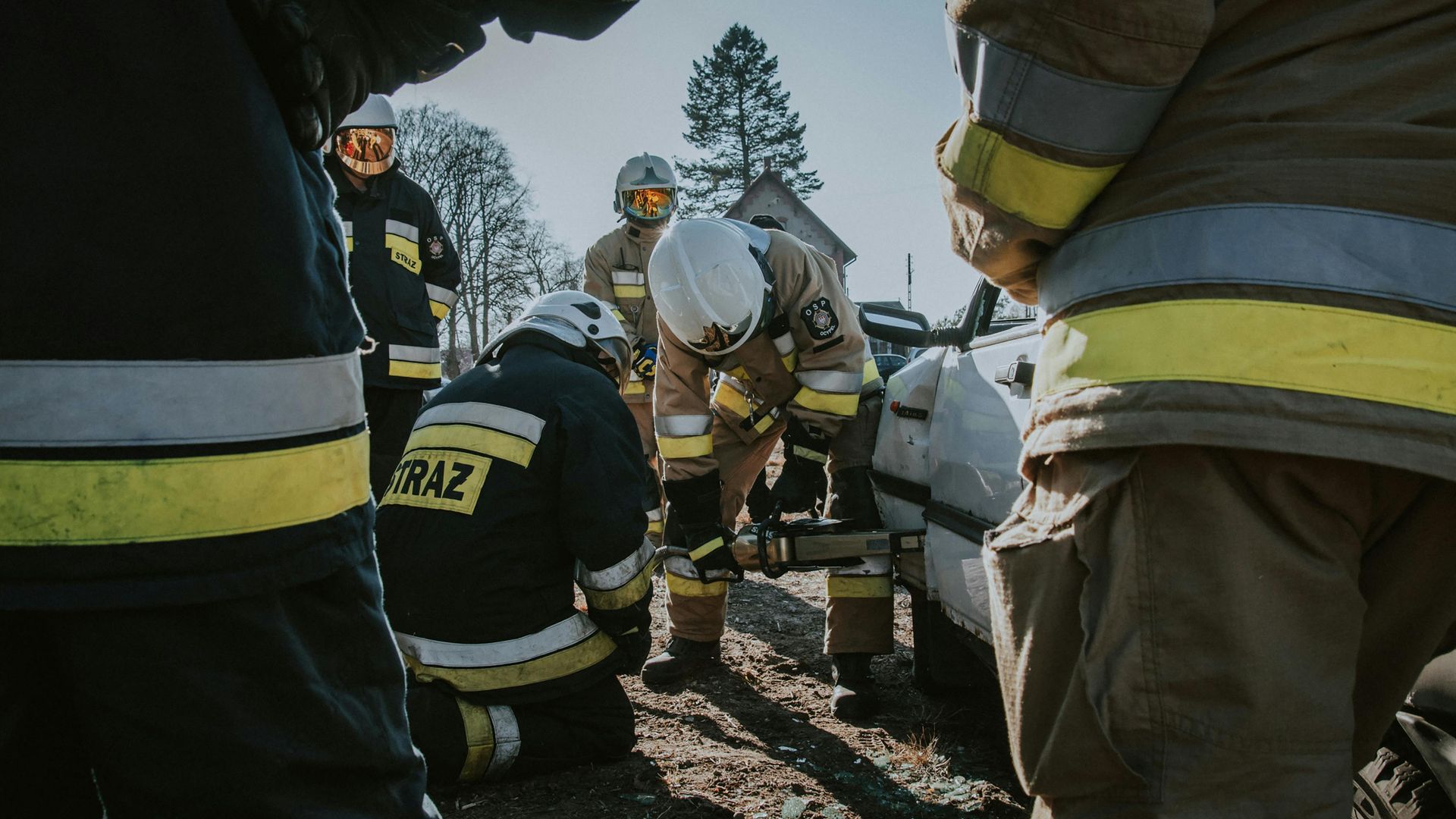 Firefighters in yellow helmets and reflective gear work together at a smoky outdoor scene.
