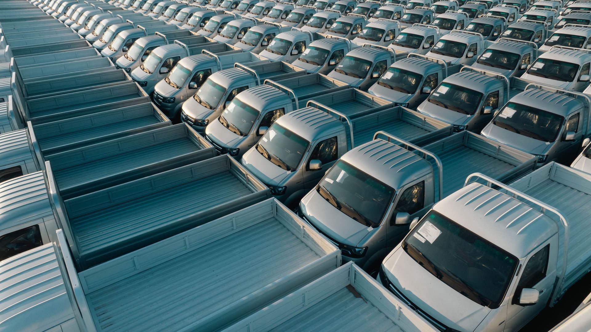 Rows of white trucks in a parking lot, seen from above.