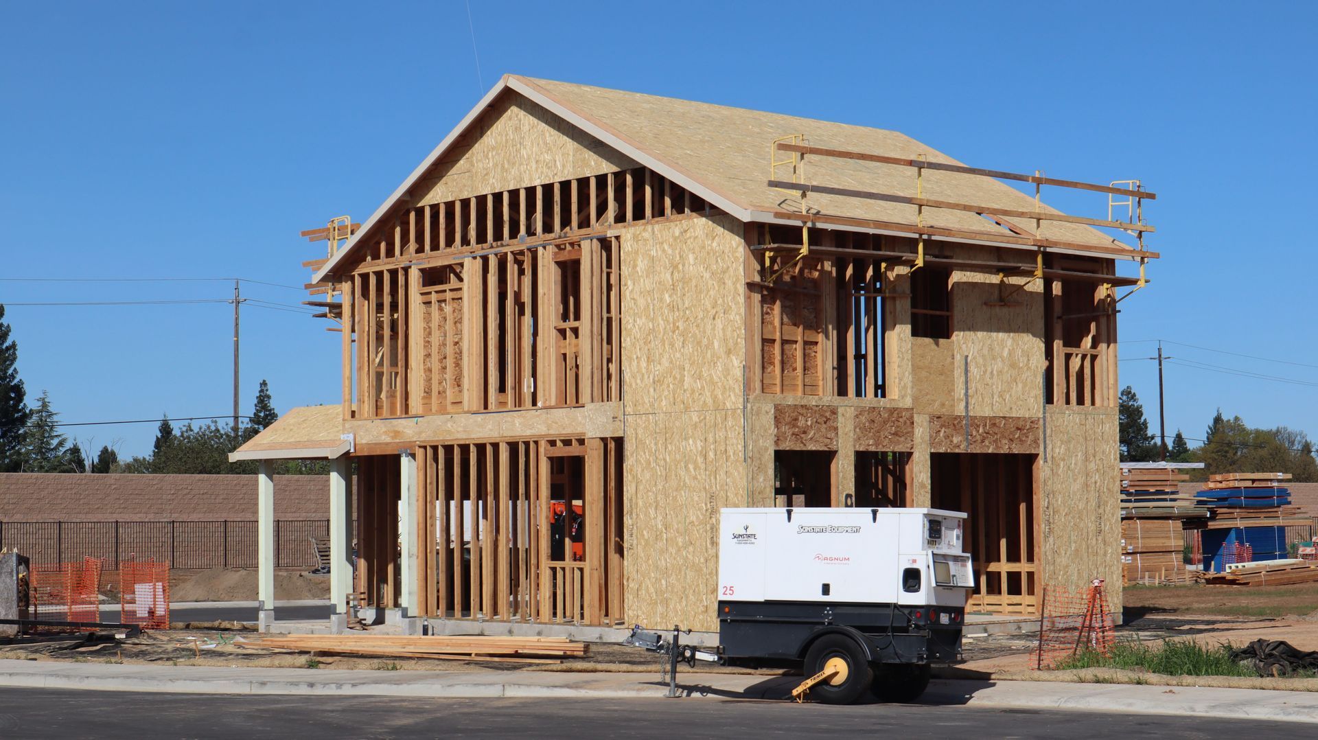 Two-story custom home in the framing stage with roof trusses in place under a clear daytime sky