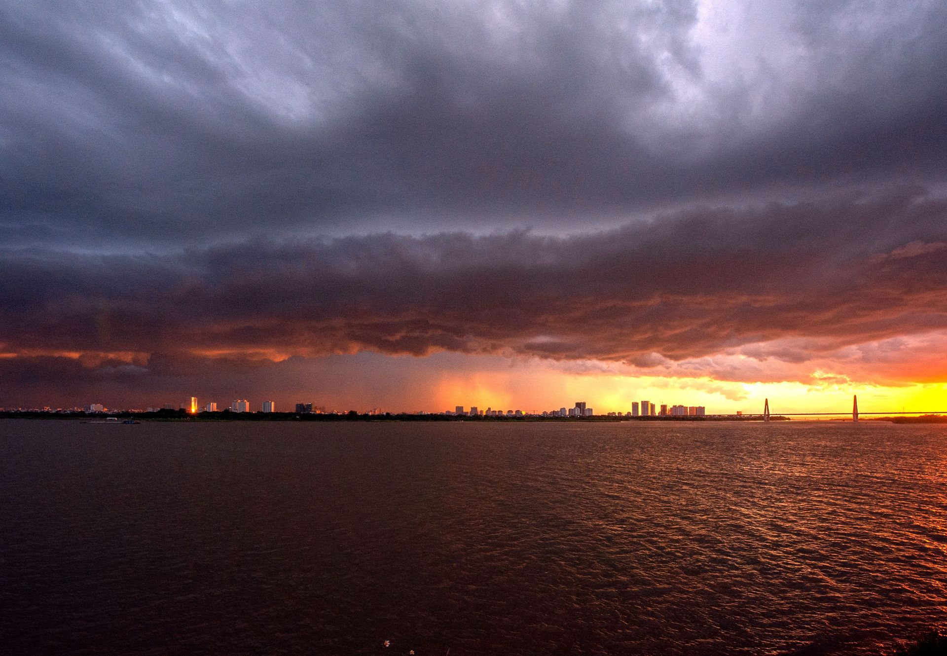 Dramatic sunset over a dark ocean with a distant city skyline and glowing orange horizon