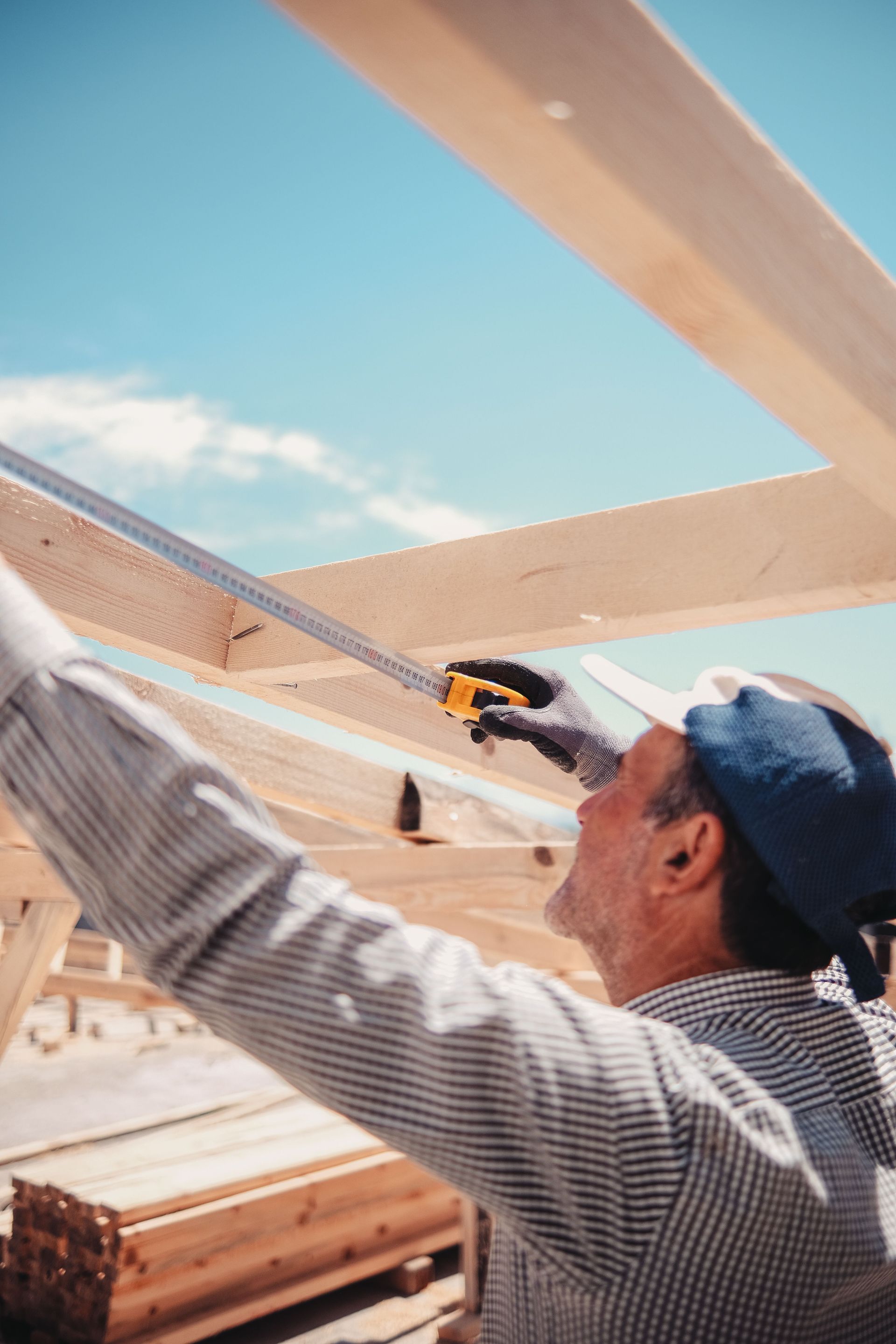 Carpenter measuring lumber on a new roof frame under a clear sky, add-a-room work to report on a Texas manufactured home