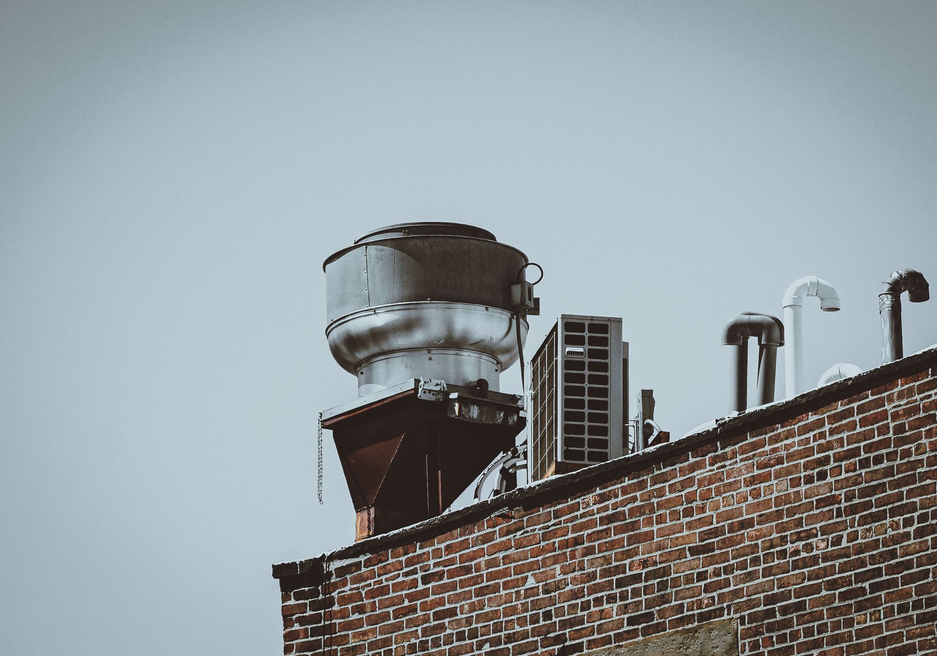 A metal rooftop exhaust fan and vent stacks on a brick commercial building, equipment that can quit