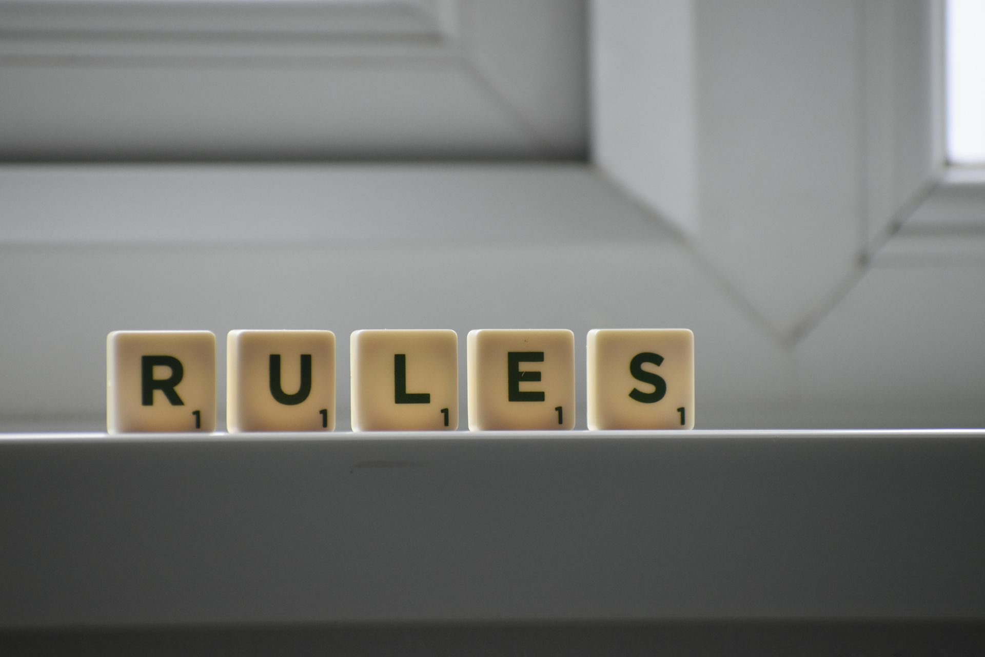 Wooden blocks spelling “RULES” on a gray shelf in front of a window.