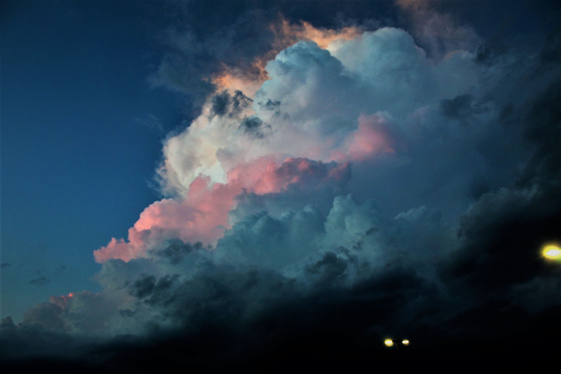 Dark storm cloud with pink-lit edges against a blue sky at dusk