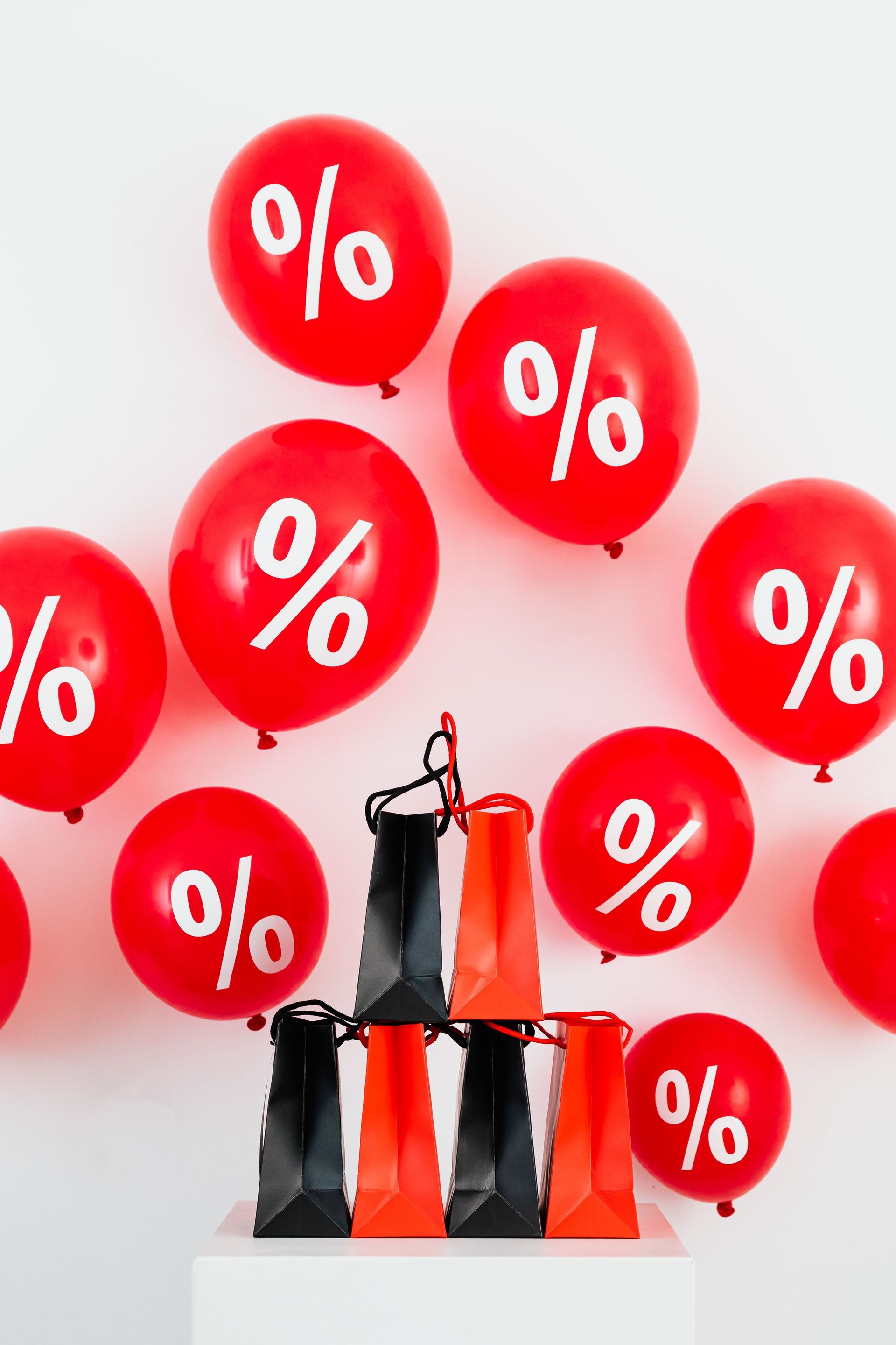 Black shopping bags beneath red discount balloons with white percent signs