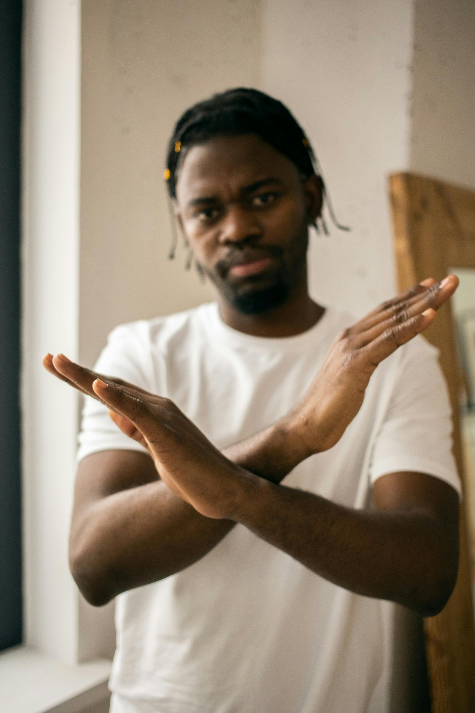 Man in a white T-shirt making an X gesture with crossed forearms indoors