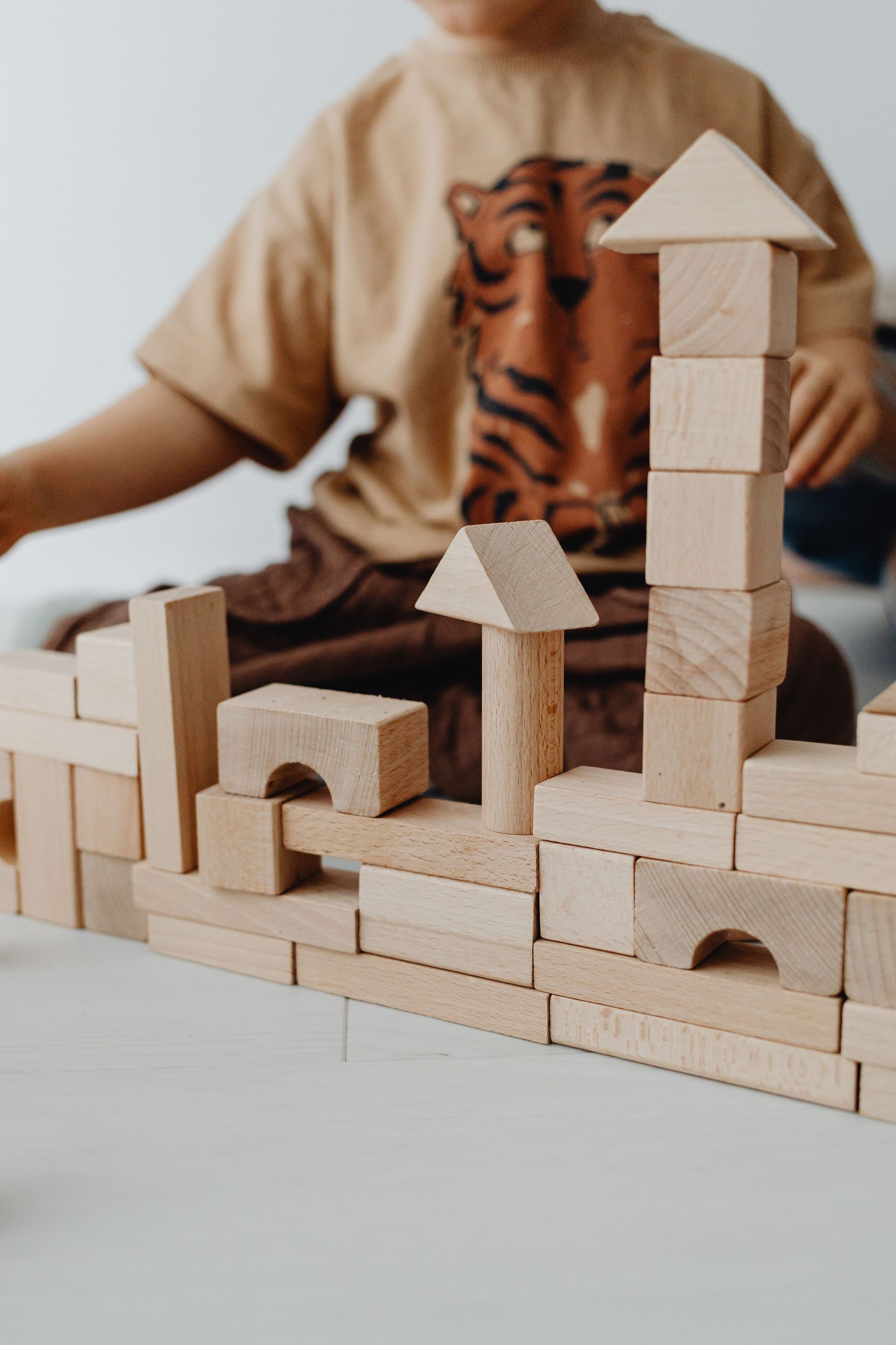 Child building a wooden block structure with towers and arches on a table