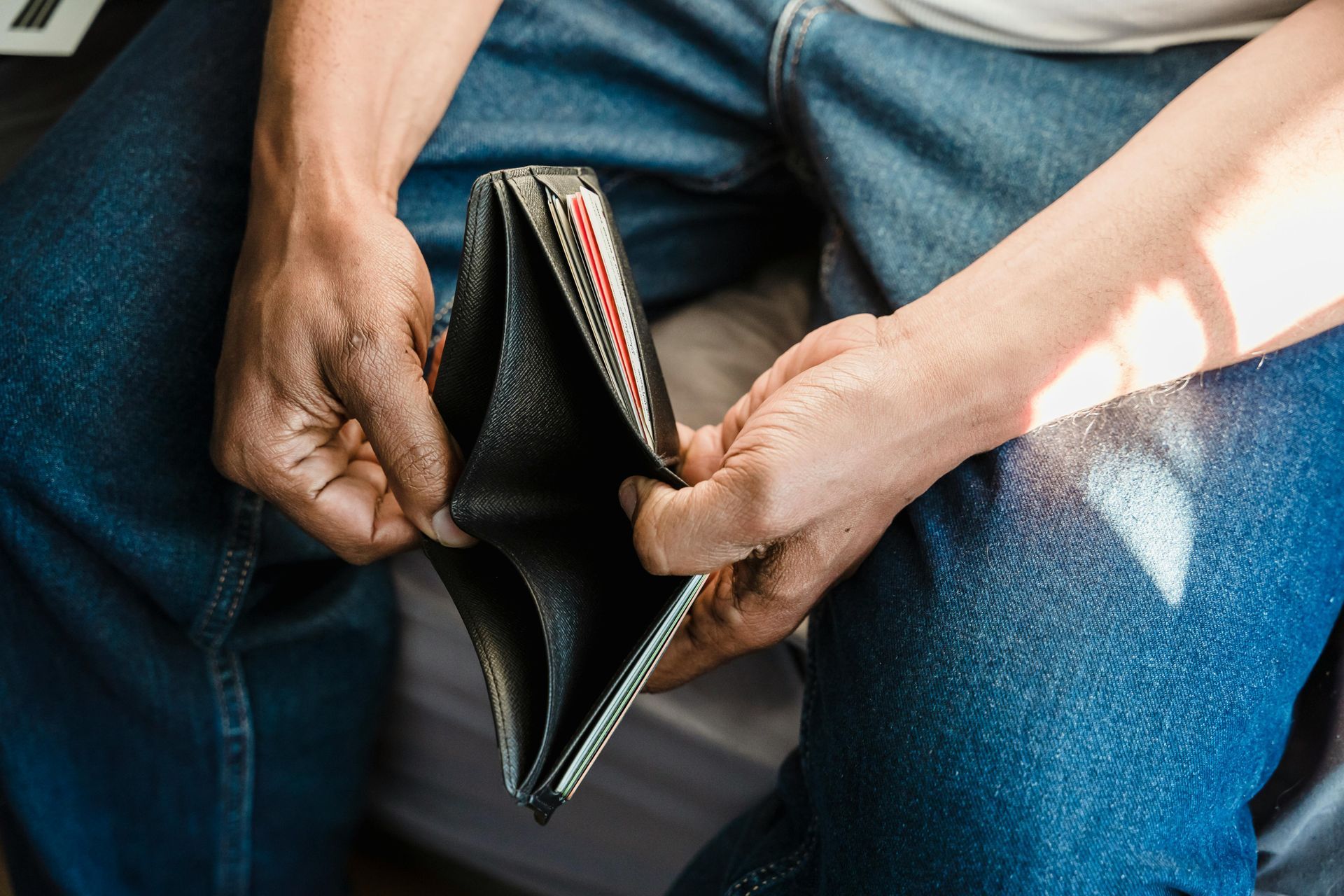 Hands holding an empty black wallet over jeans, suggesting financial strain.