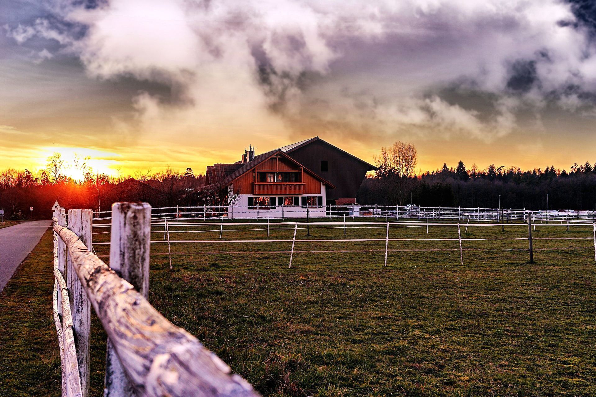 Wooden ranch fence line along a rural Texas pasture at sunset with a barn in the distance behind it