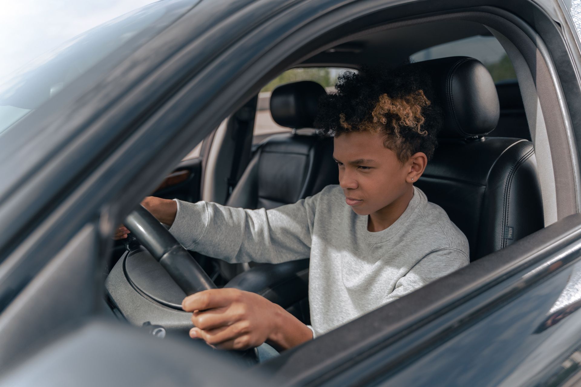 Teenage driver behind the wheel of a car, seen through the open driver's window
