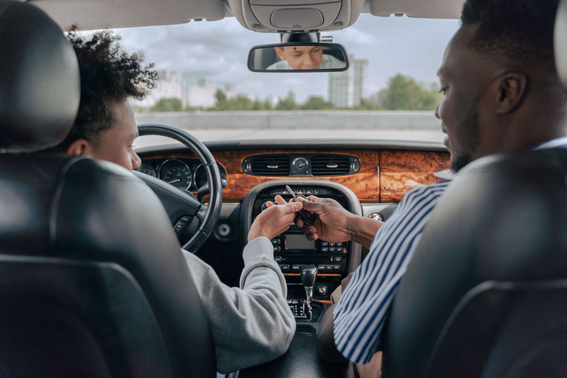 Parent handing car keys to a teenage driver in the front seat of a family car