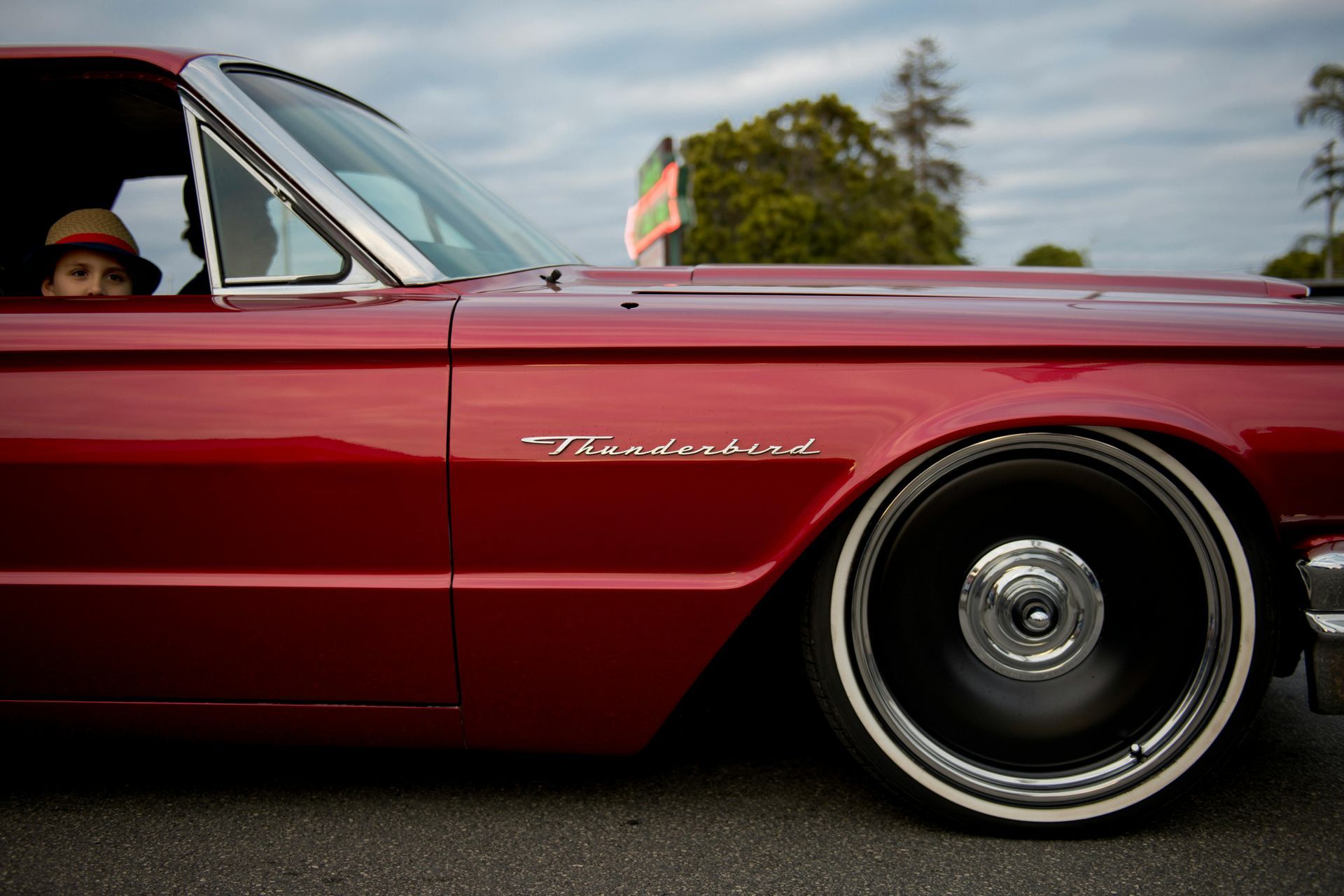 Red classic car side view with whitewall tire and a driver wearing a hat
